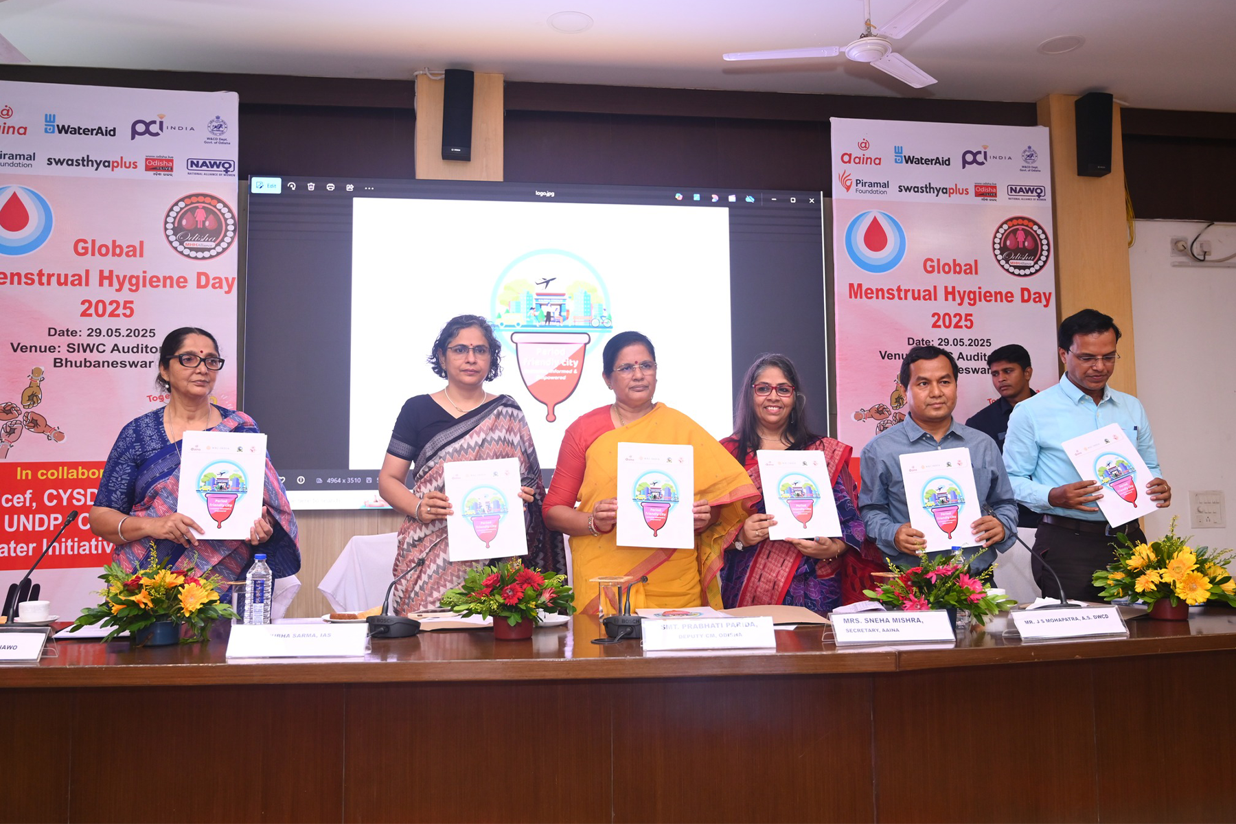 6 people stand behind a table and hold up posters with a menstual cup.