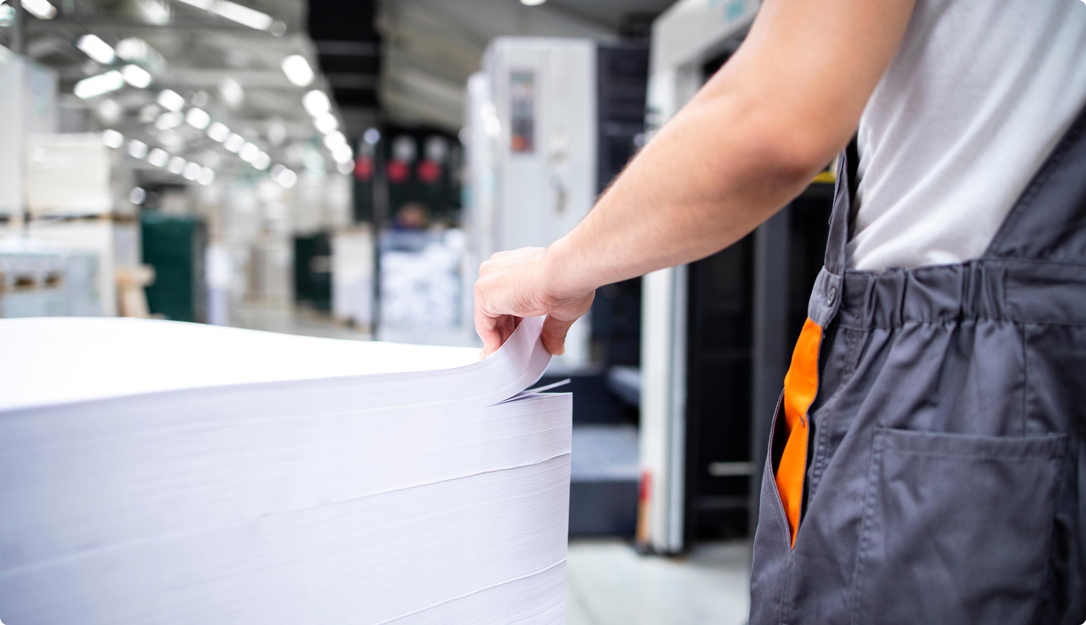 Photo d'une pile de papier blanc dans une usine de pâtes et papiers avec la main d'un travailleur.