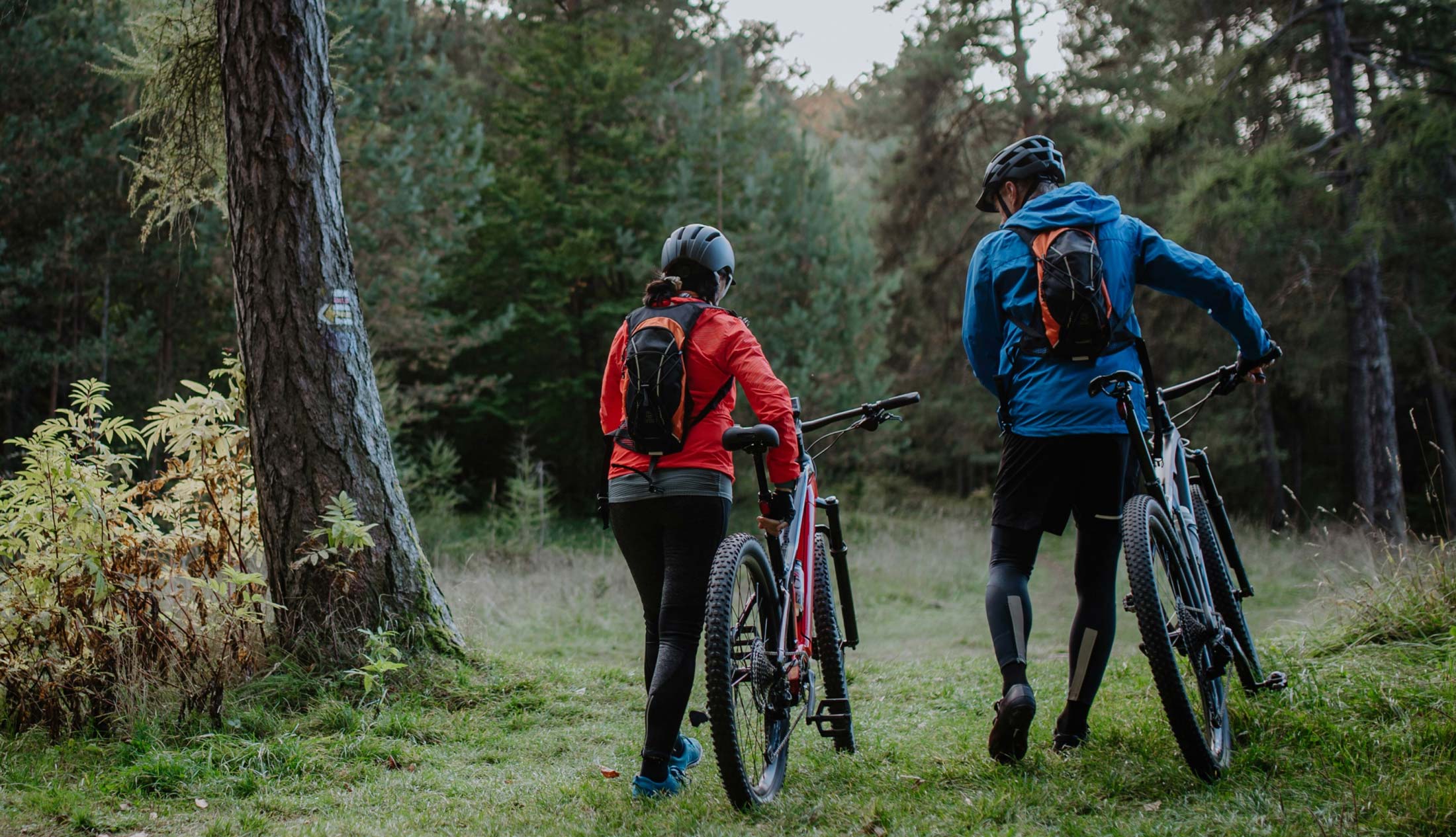 Two people holding their e-bike in the forest.