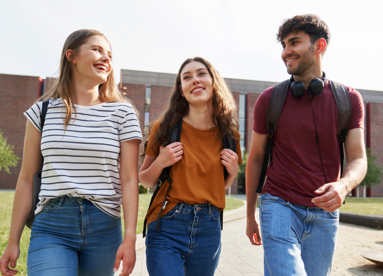3 young adults with backpacks smiling outside school