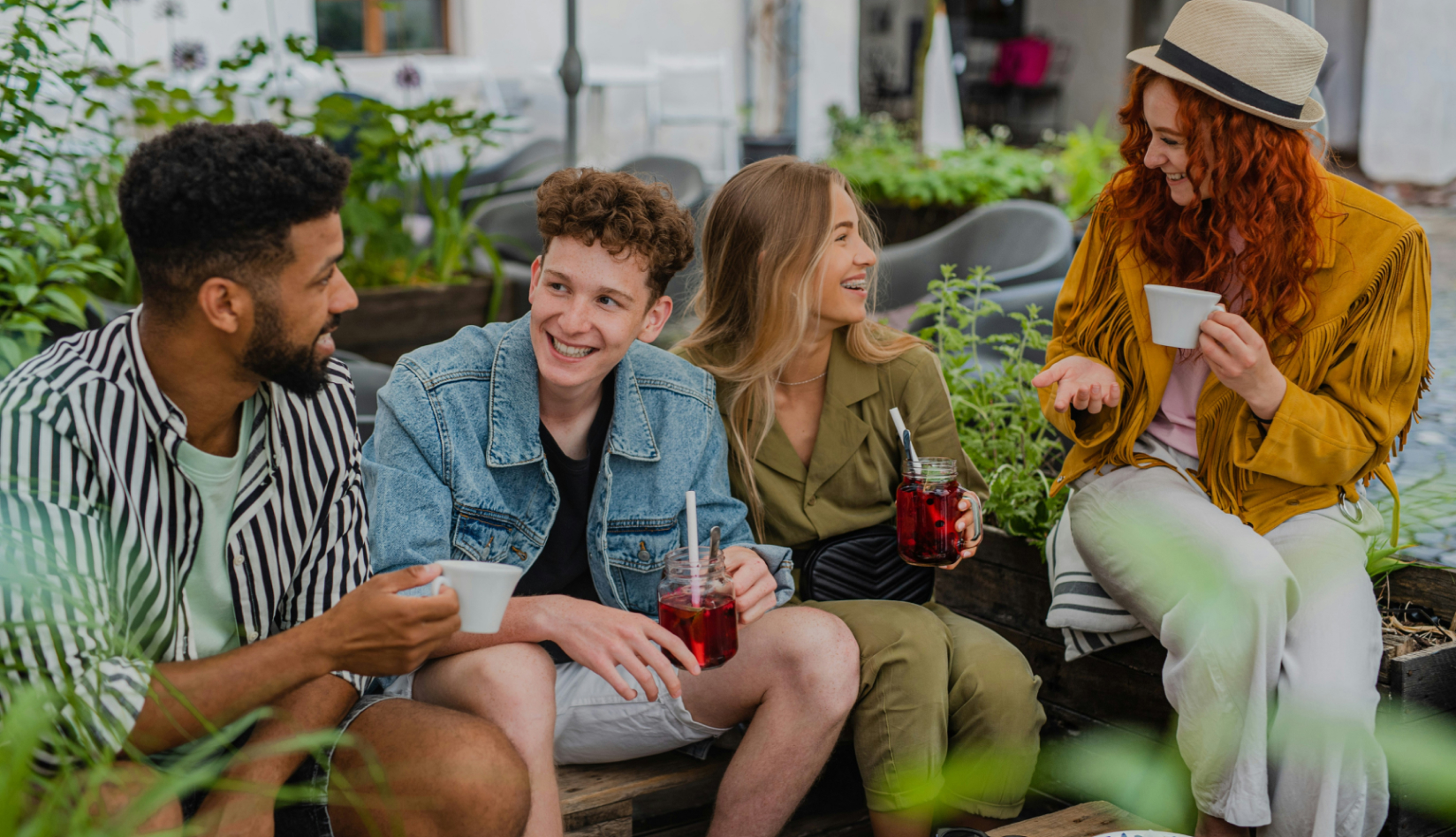 4 young adults sitting and smiling having coffee and juice together
