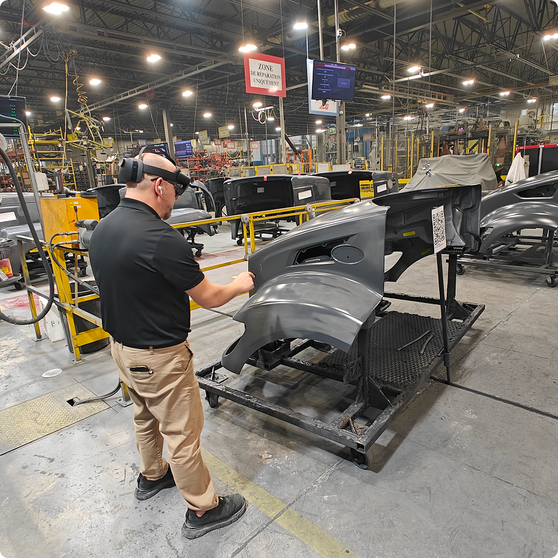 A worker in a factory wearing the AR Microsoft HoloLens and using the app to identify defaults on a bumper.