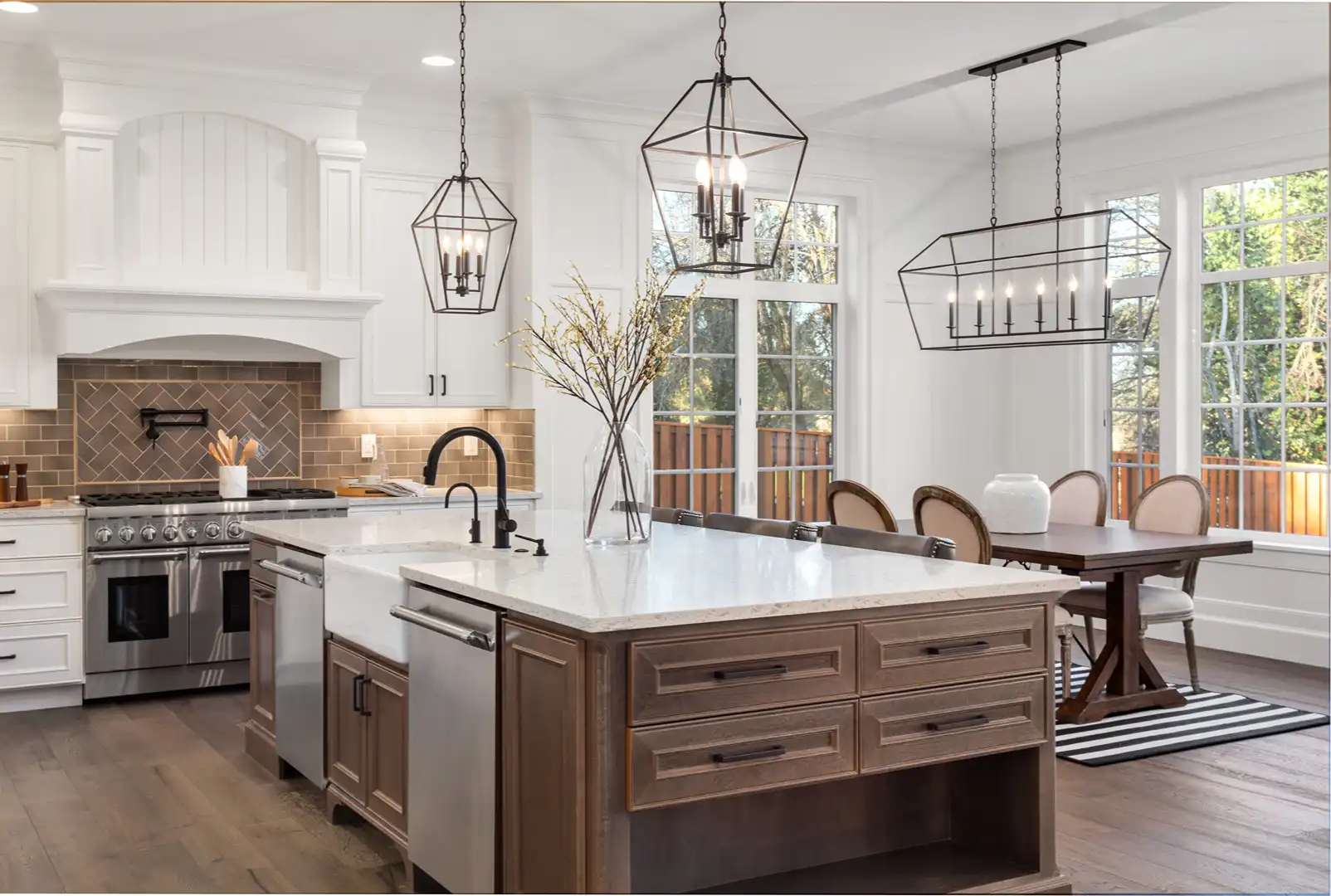 Bright kitchen with white cabinets, brown island, stainless appliances, and large windows by dining area.