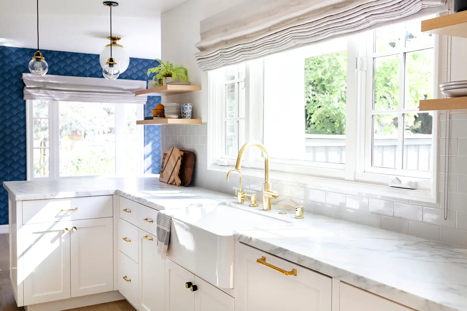 Bright kitchen with white cabinets, marble countertops, gold faucet, and blue patterned wall.