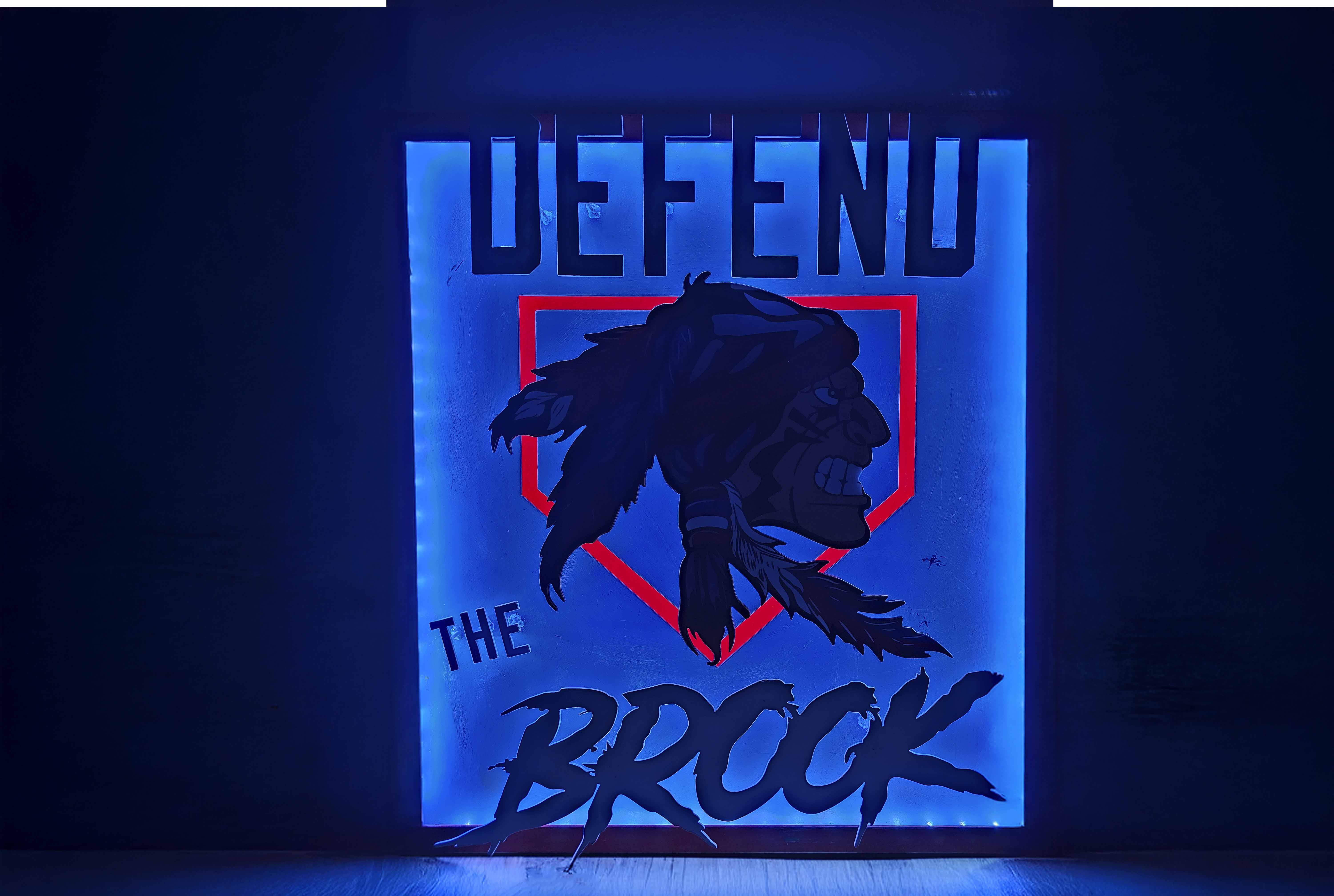 Illuminated sign with text 'DEFEND THE BROCK' and a profile illustration of a Native American face with feathers.