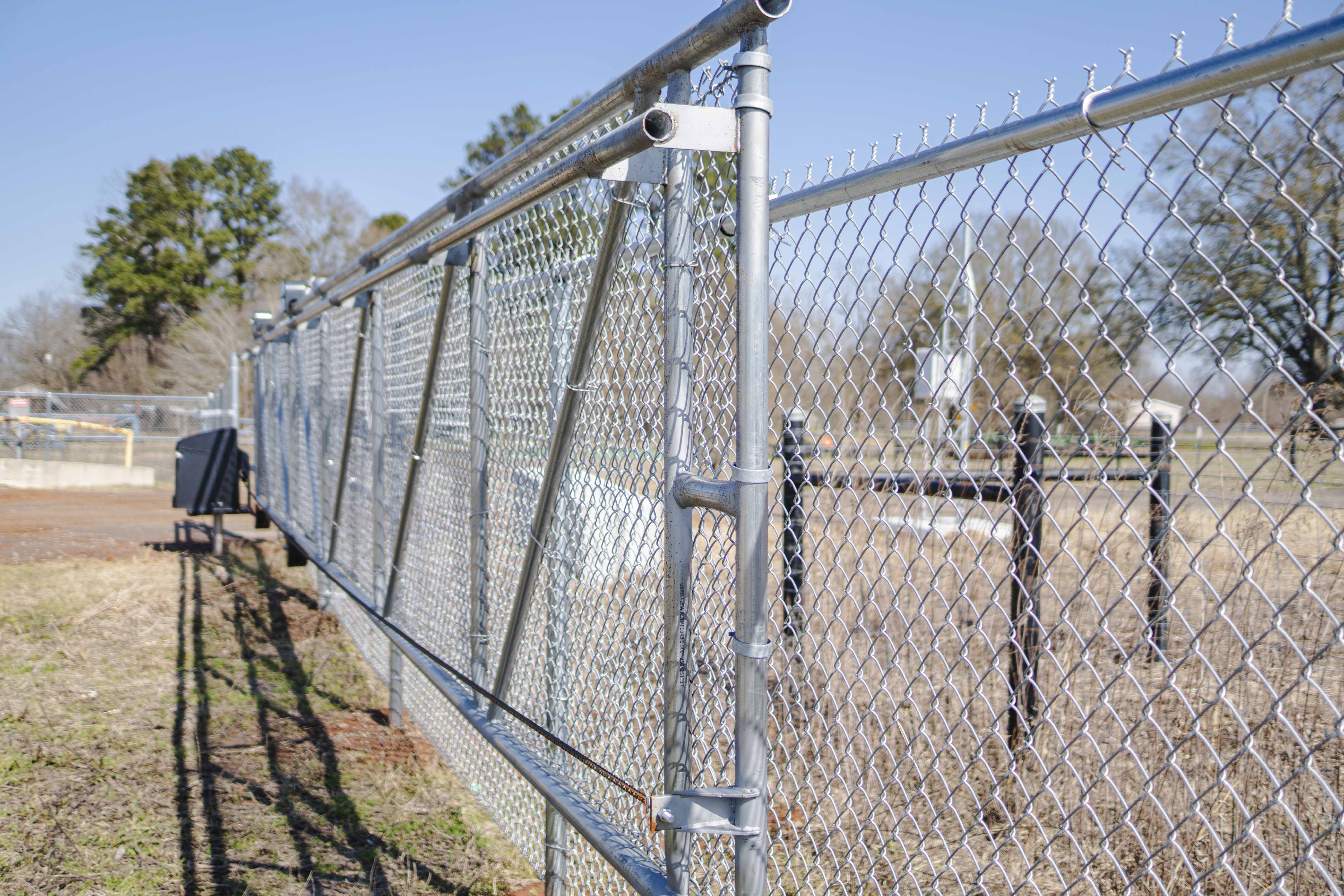 Close-up view of a silver chain-link fence running along grassy ground under a clear blue sky.