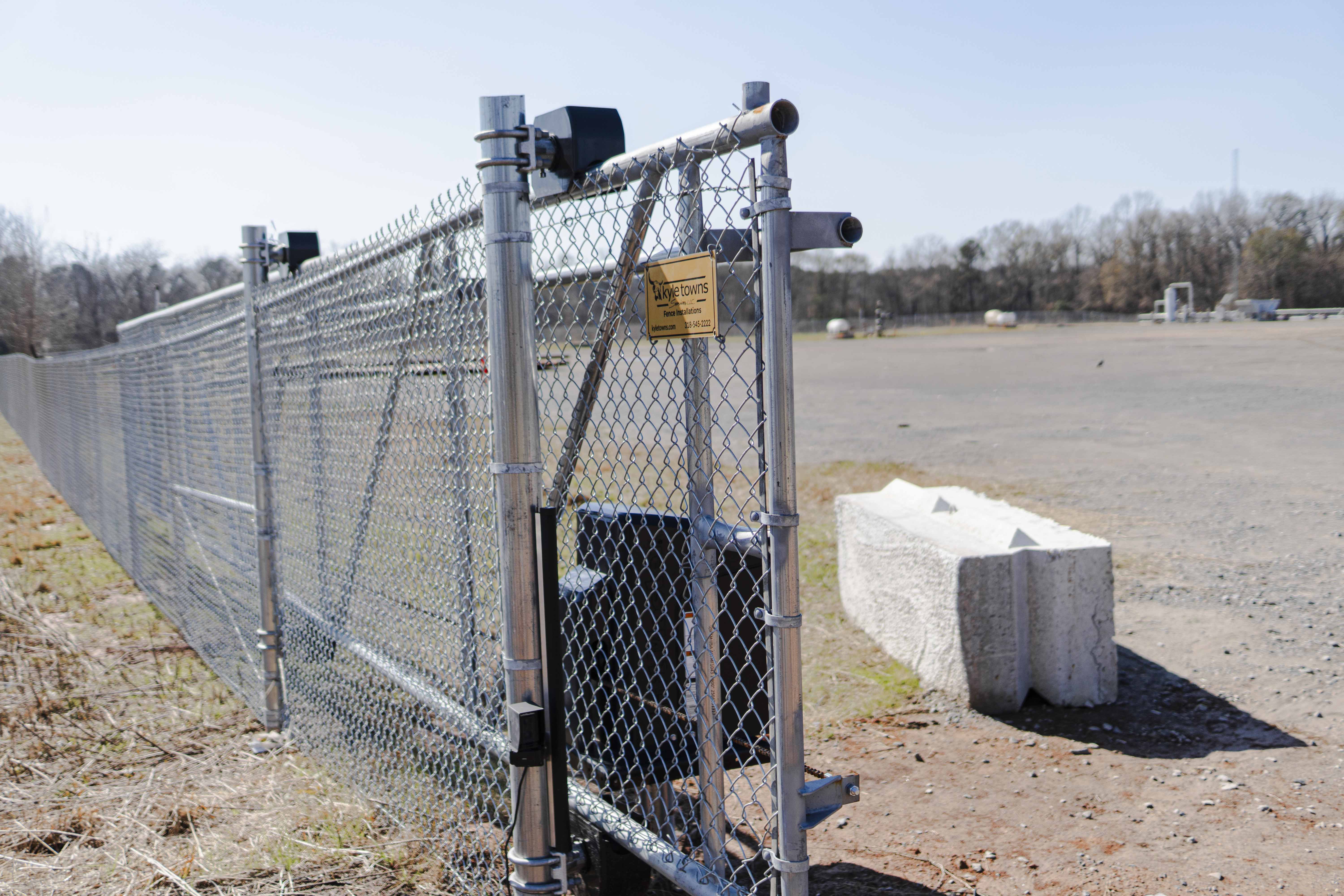 Metal chain-link fence with a gate and a sign reading 'kyletowns Fence Installations' next to an open gravel area.