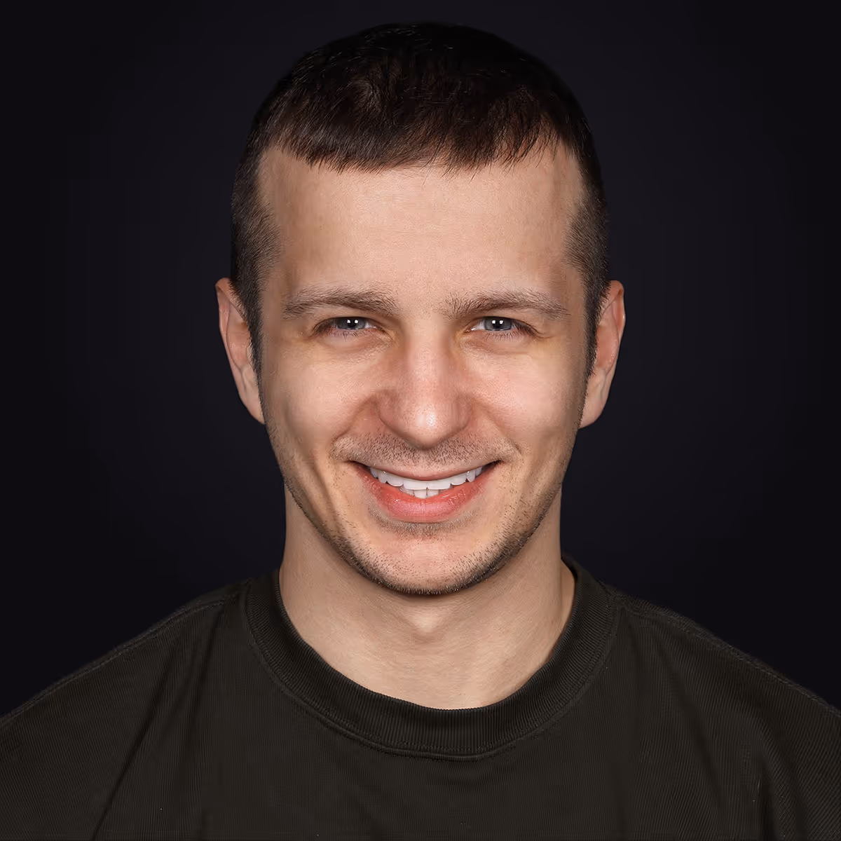 Олександр — пацієнт із керамічними реставраціями, усміхнений чоловік на темному фоні.