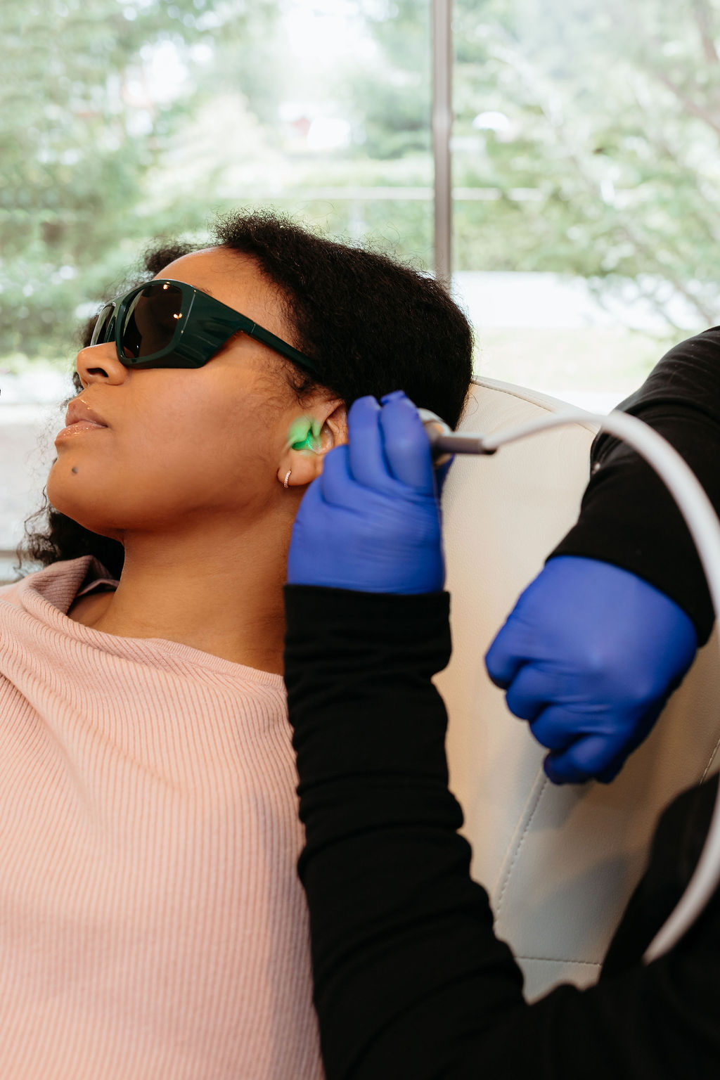 Close-up photo of a woman's face receiving red light therapy, highlighting the glow on her skin, with a look of relaxation