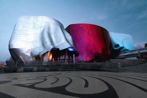MOPOP exterior, with silver, purple/red, and blue and organically shaped metal. The monorail is visible, protruding from the right hand side of the image. A gray maze is also visible in front of the museum