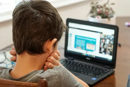 A white boy looking at a small laptop screen
