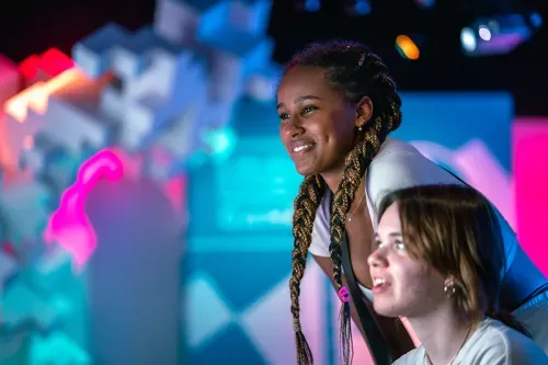 A Black woman and white teenager looking at a screen and smiling in the Indie Game Revolution video game exhibition