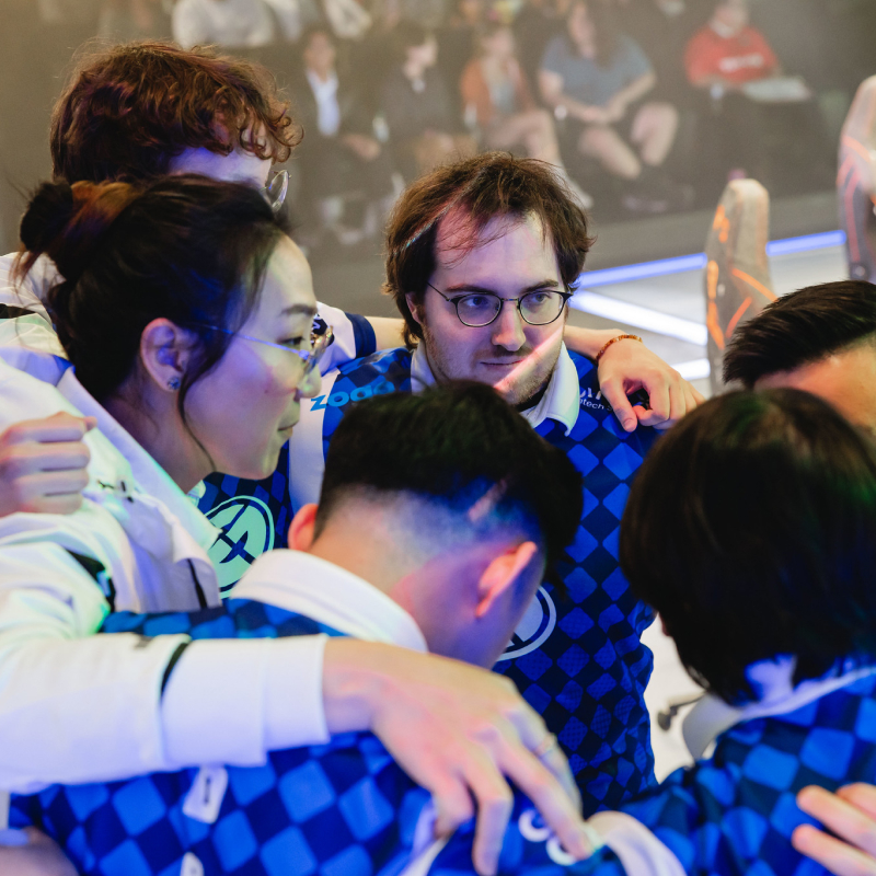 An interracial e-sports team huddles, dressed in uniform