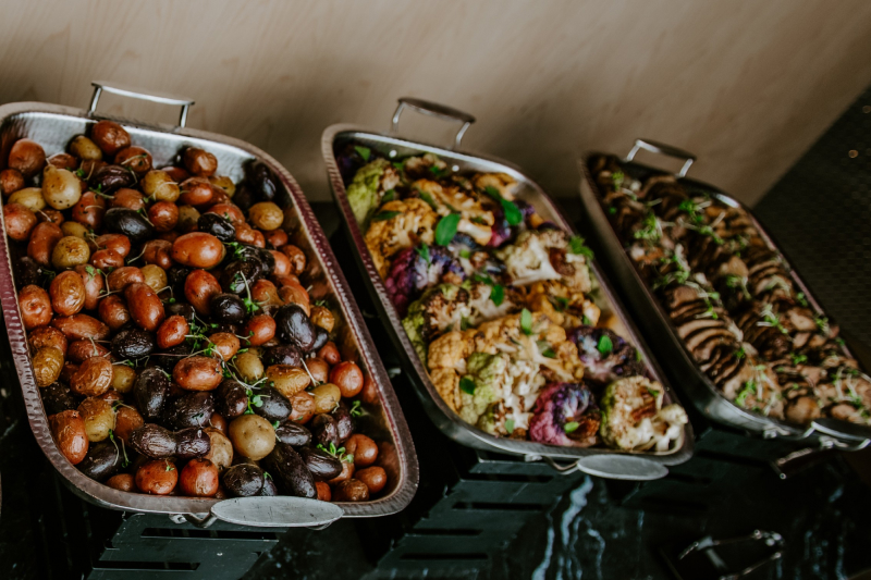 Three trays of roasted vegetables including assorted baby potatoes, grilled cauliflower with herbs, and sliced mushrooms.