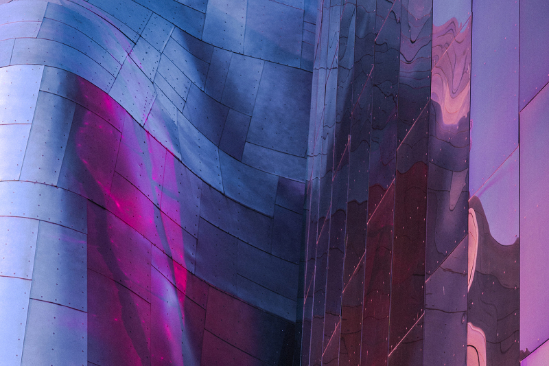 Curved metallic building facade with reflective purple and pink light.