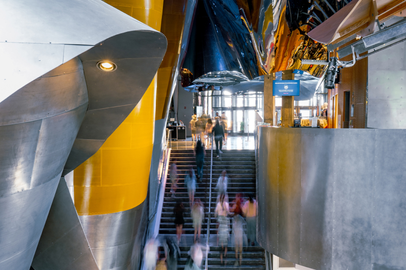 People ascending and descending a staircase inside a modern building with large metal and yellow architectural features.