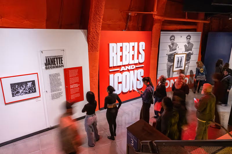 People viewing the Rebels and Icons exhibition with photography and large red sign indoors.