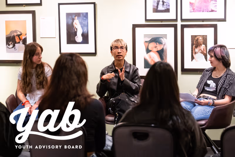 Youth Advisory Board members engaged in discussion seated in a room with framed photos on the wall.