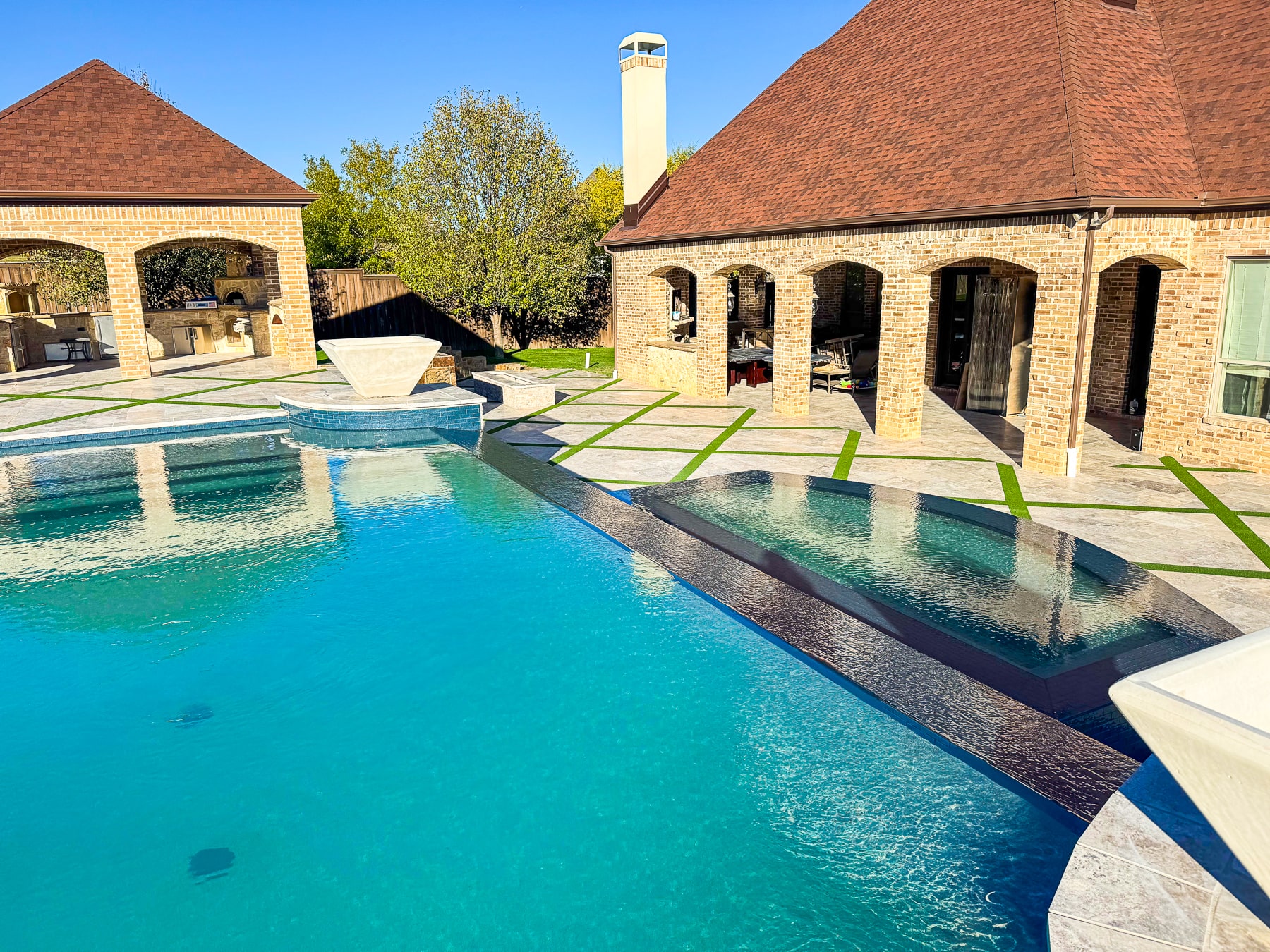A large pool adjacent to a backyard patio made of bricks attached to a house. 