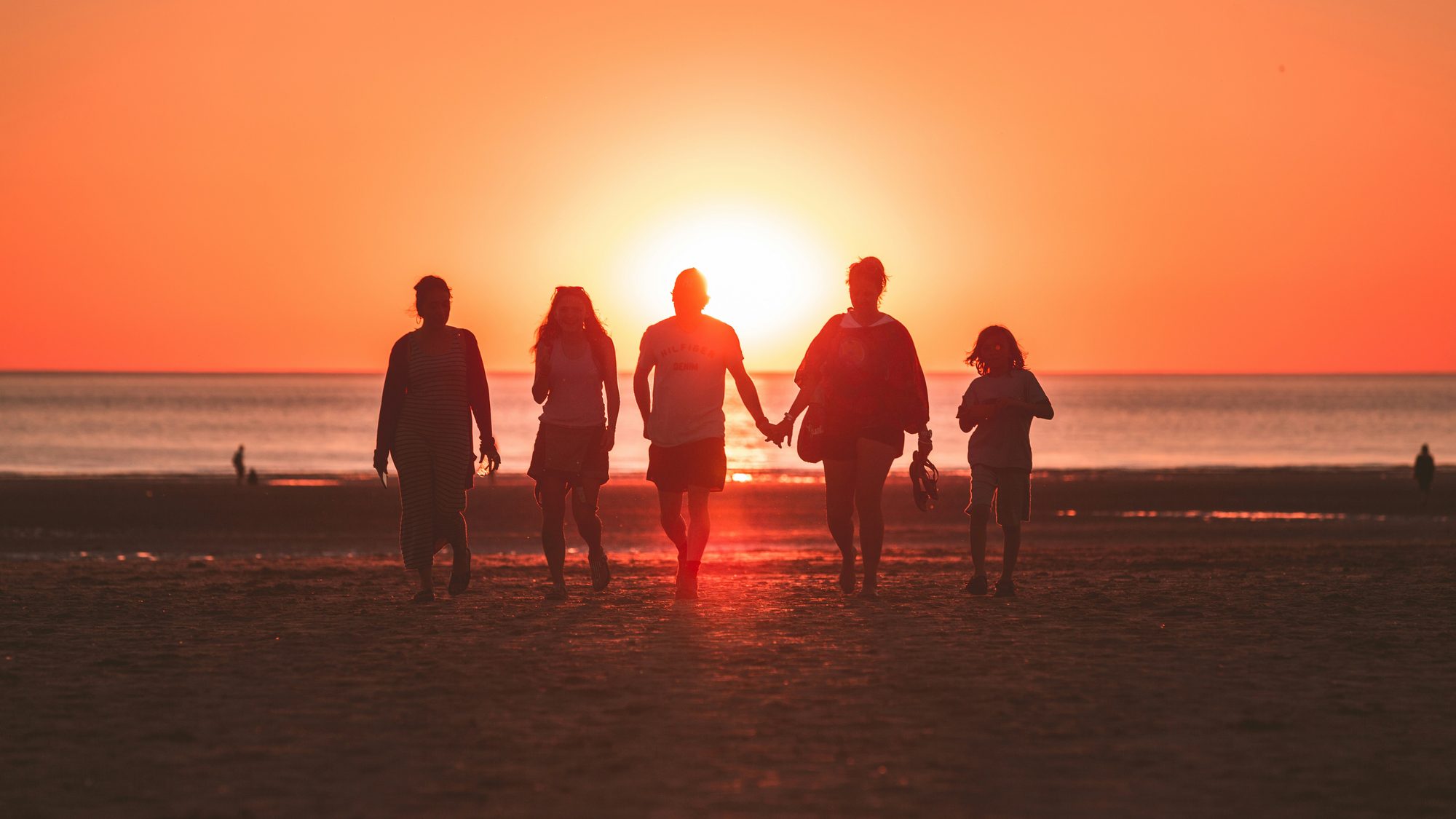 A family silhouetted together on the beach at sunset