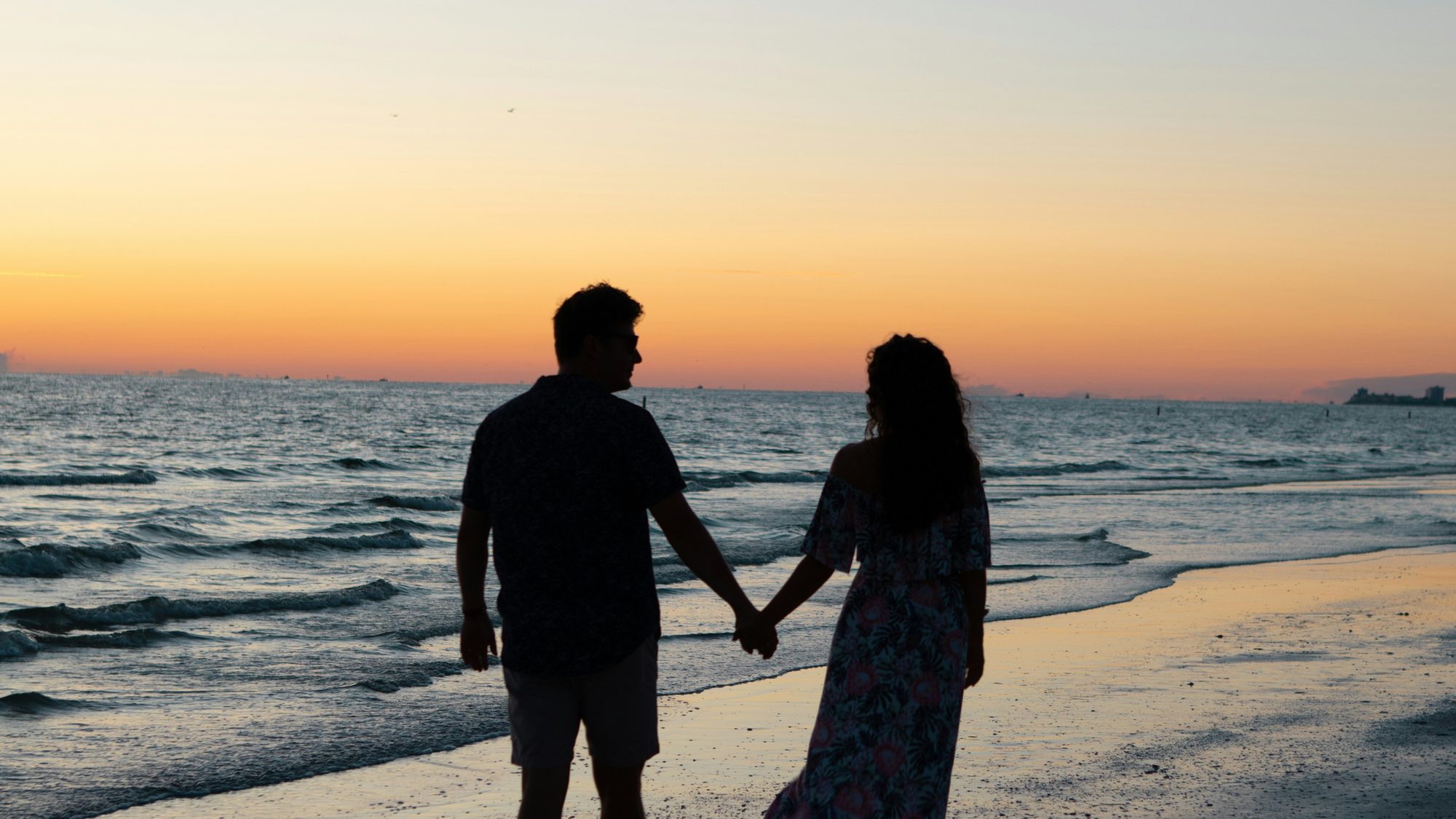 A couple walking together along the shoreline at sunset