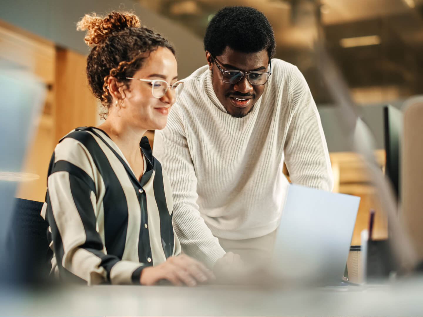 Two colleagues collaborate at a desk, reviewing information on a laptop in a modern office setting.