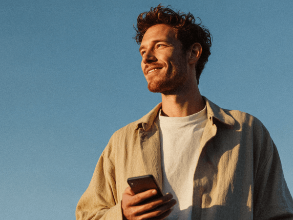 Man holding a smartphone outdoors, looking forward against a clear blue sky
