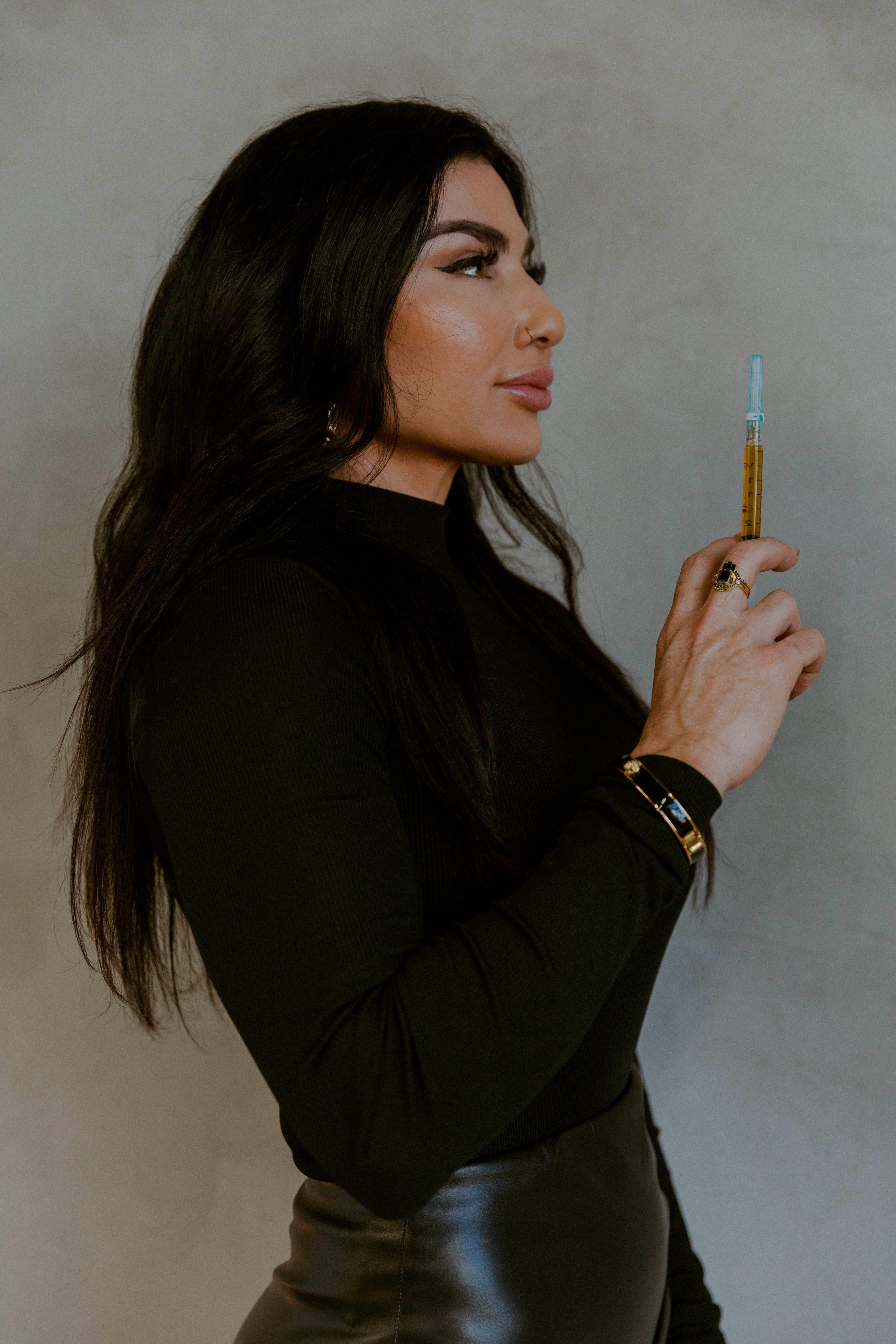 Five women posing indoors against a plain wall, wearing mostly black outfits with one in a white top, sitting and standing on stools.