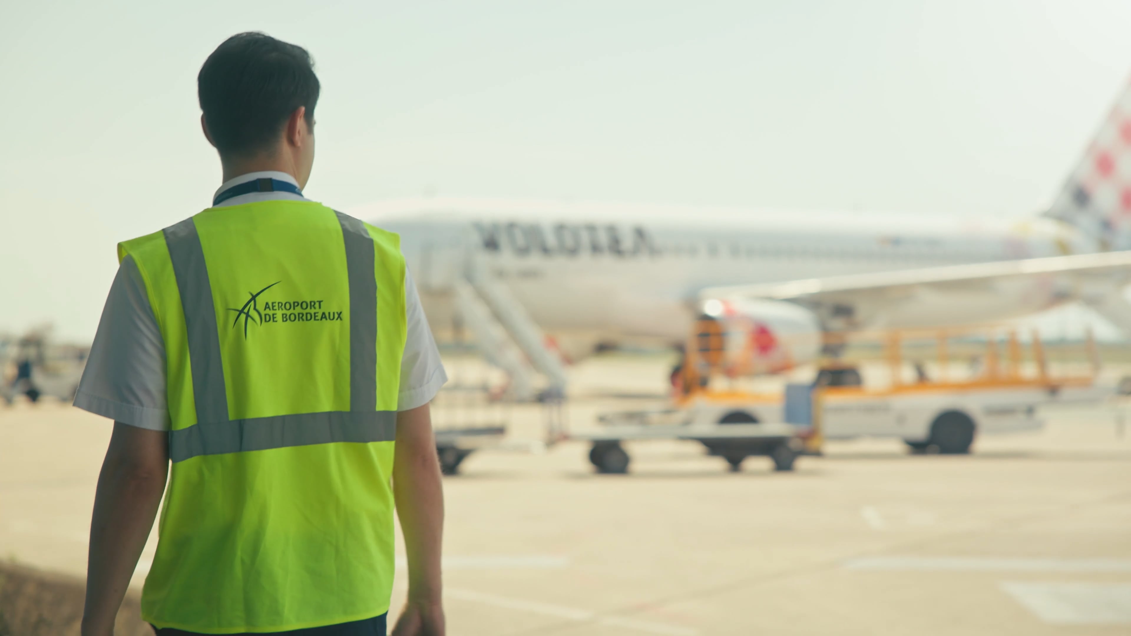 Employé de l'aéroport de Bordeaux portant un gilet de sécurité jaune, debout devant un avion au sol.