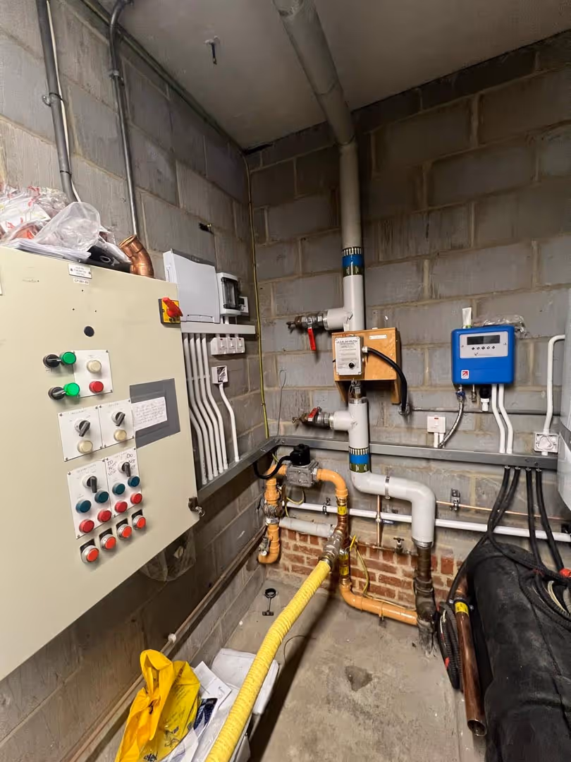 A small utility room with control panels, pipes, and various technical equipment on the walls.