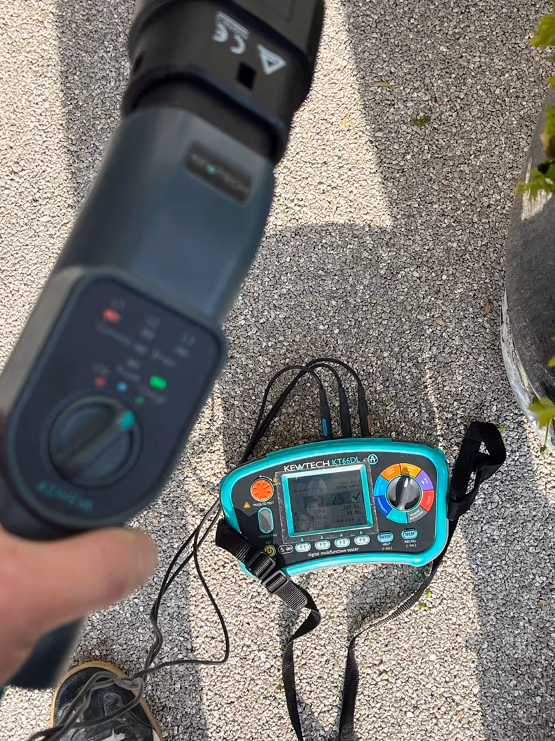 A person holds a handheld device above an electrical testing machine placed on the ground.