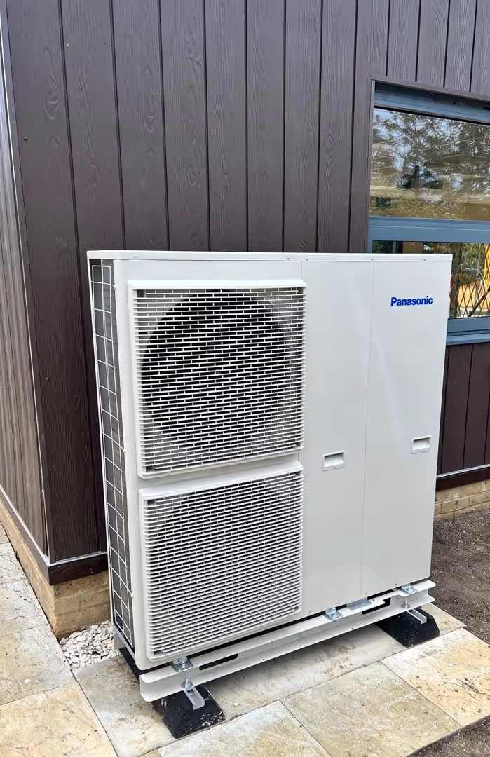 A white outdoor air conditioning unit mounted against a brown building wall.