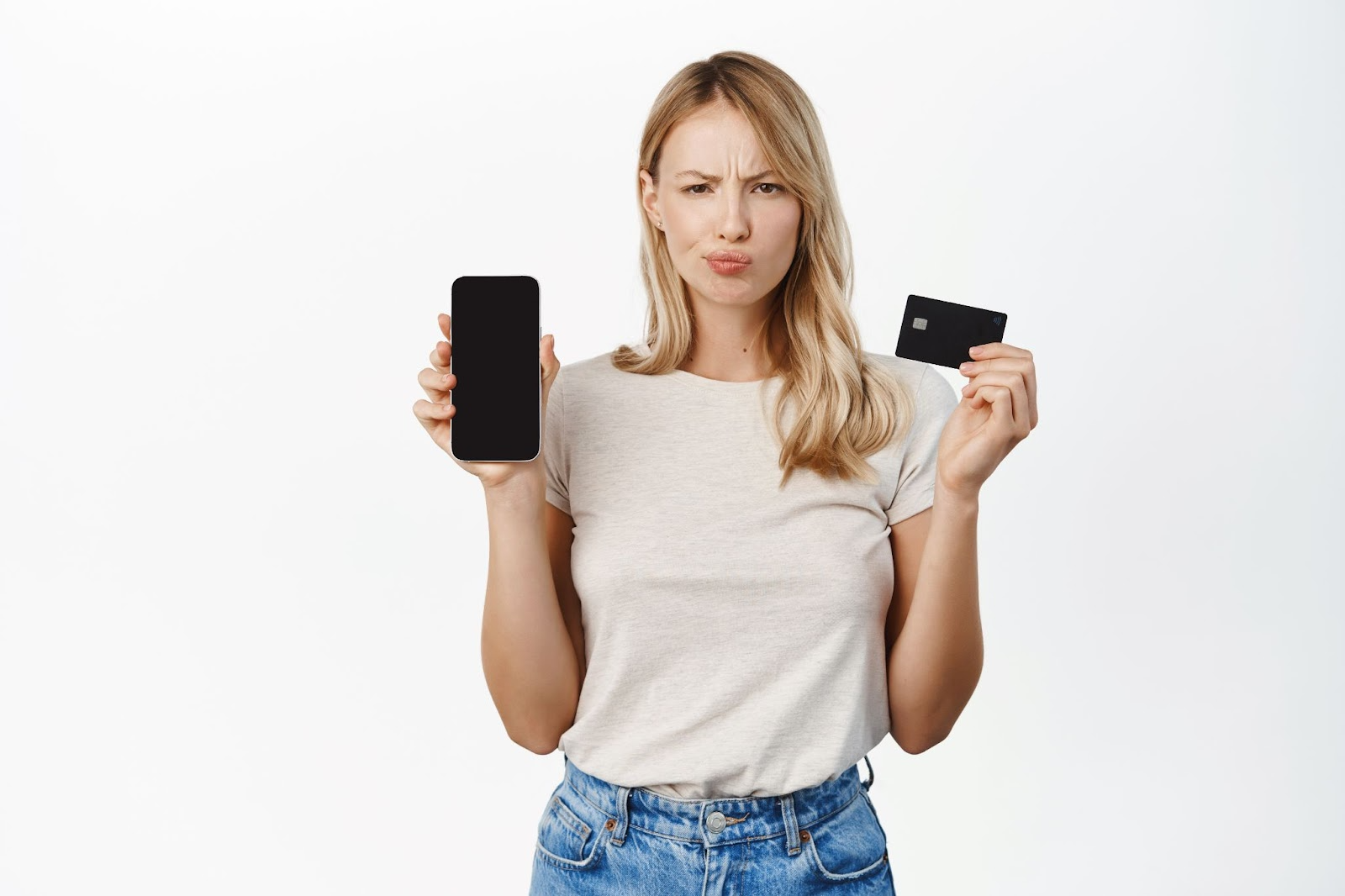 Woman holding up a cell phone on one hand and a credit card on the other hand with confused expression on her face.