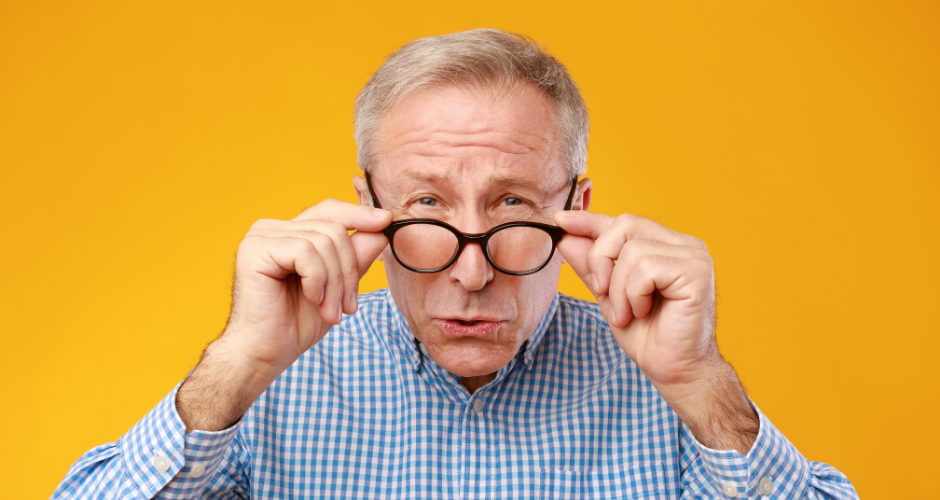 Gray-haired man squinting as he looks through his eyeglasses.