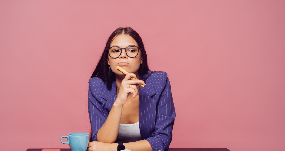 Young woman with glasses with expression that she is thinking. Has pencil on her chin as she thinks.