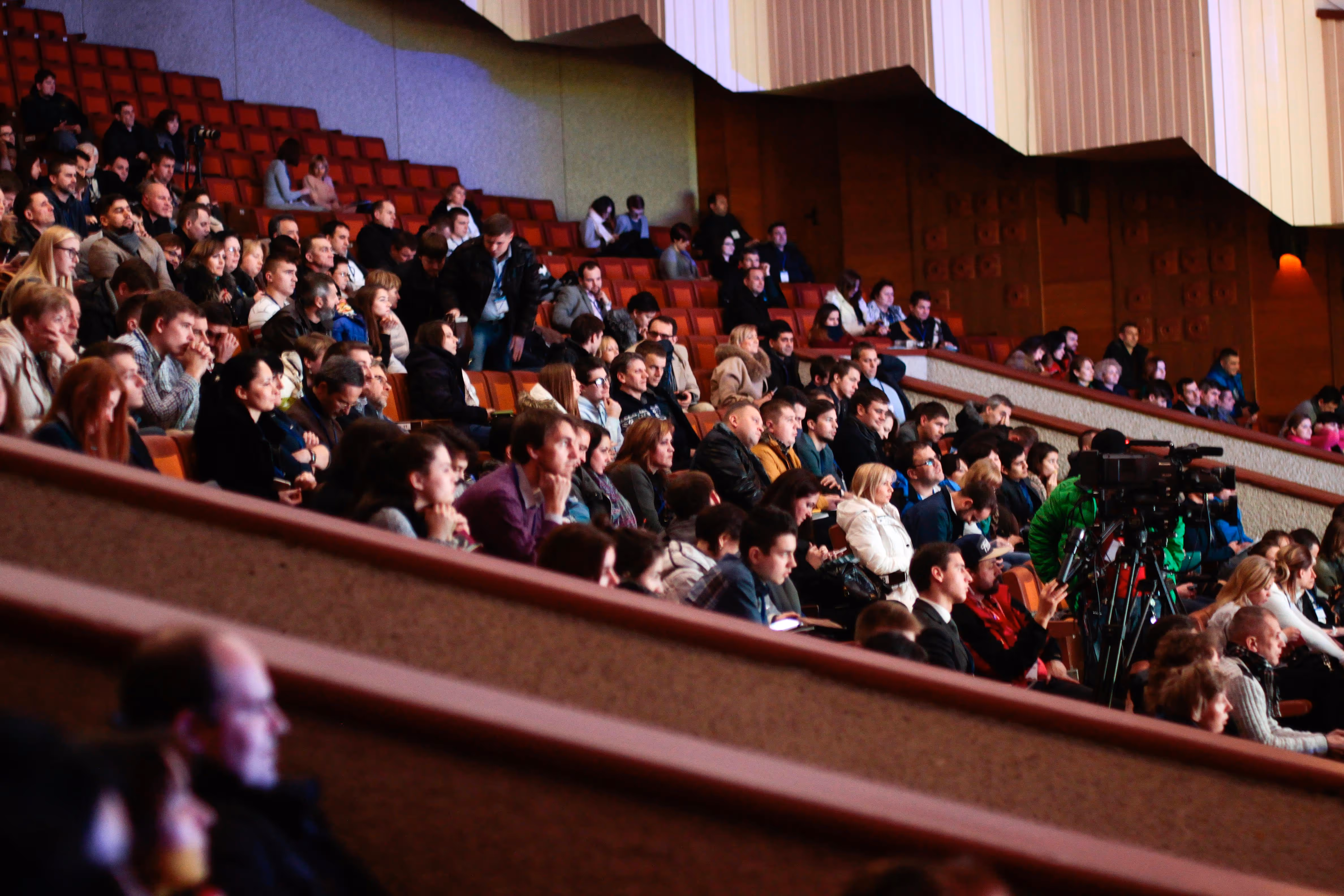 Audience seated in an auditorium, with a camera set up for recording.