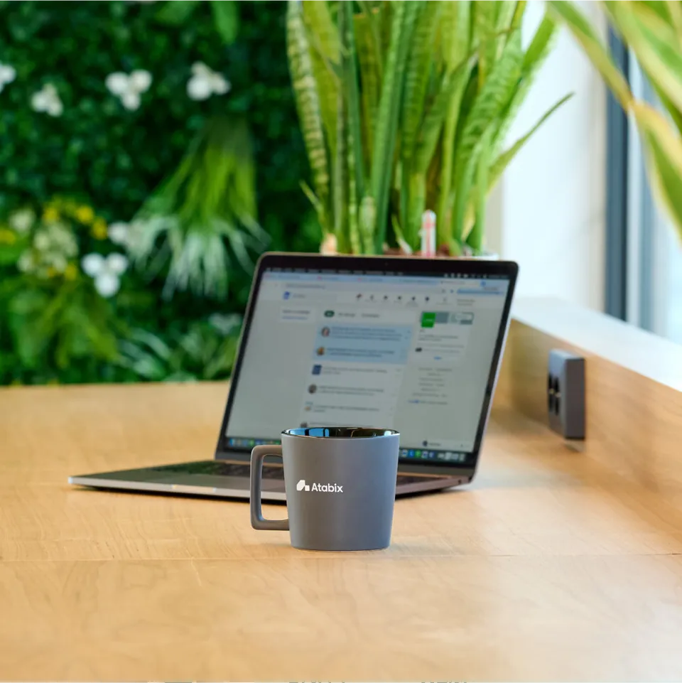 Een laptop met daarvoor een mok met het Atabix logo erop. In een kantoor ruimte met veel planten.