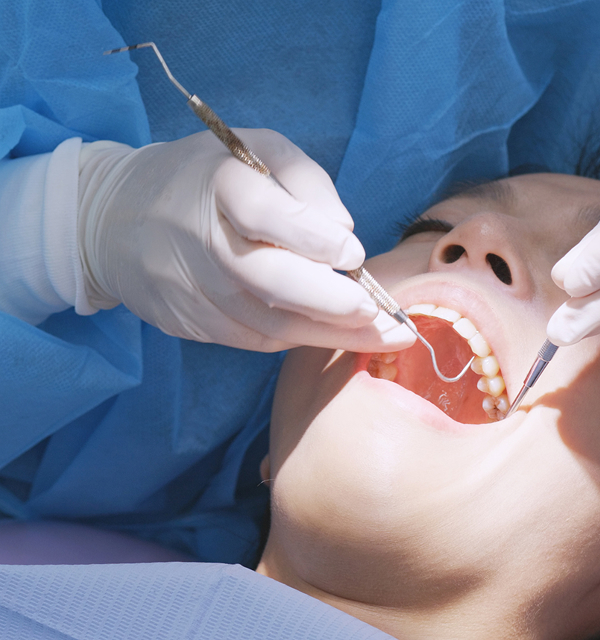 Dentist wearing gloves examines a patient's teeth with dental tools inside the mouth.