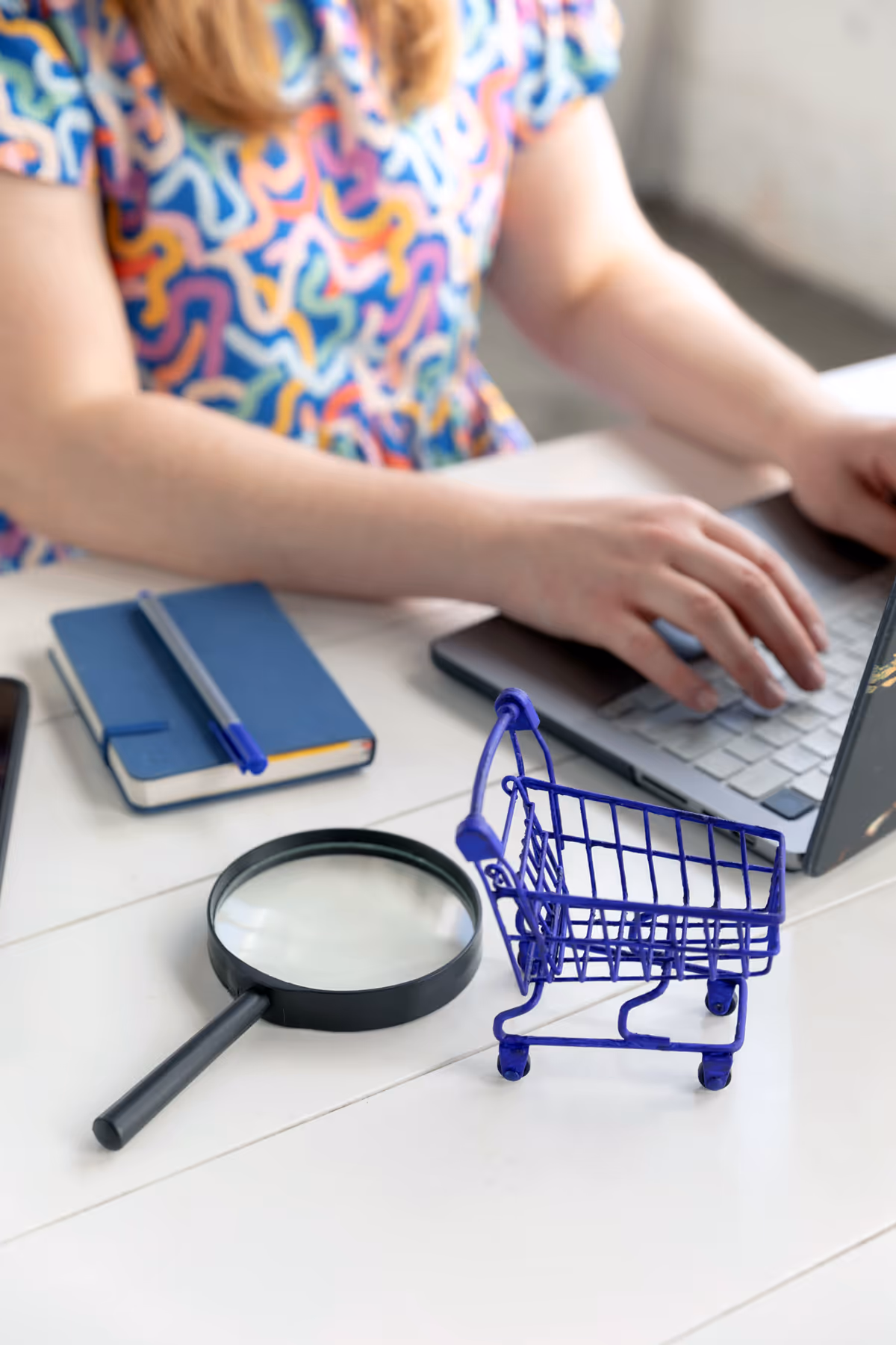 Sjammon typing on laptop, a magnifying glass and mini shopping trolley sitting on the desk.