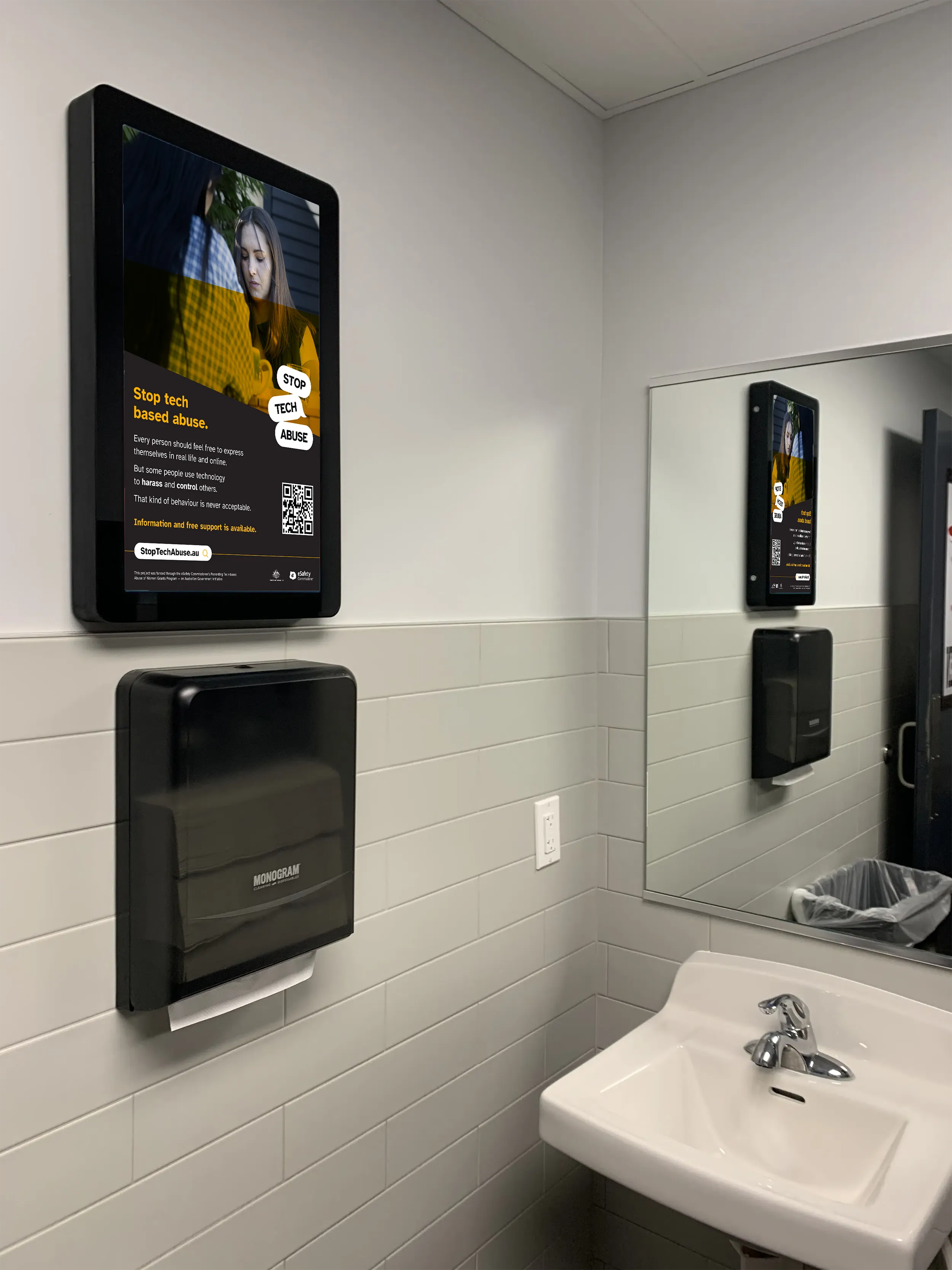 Stop Tech Abuse poster displayed above a paper towel dispenser in a bathroom