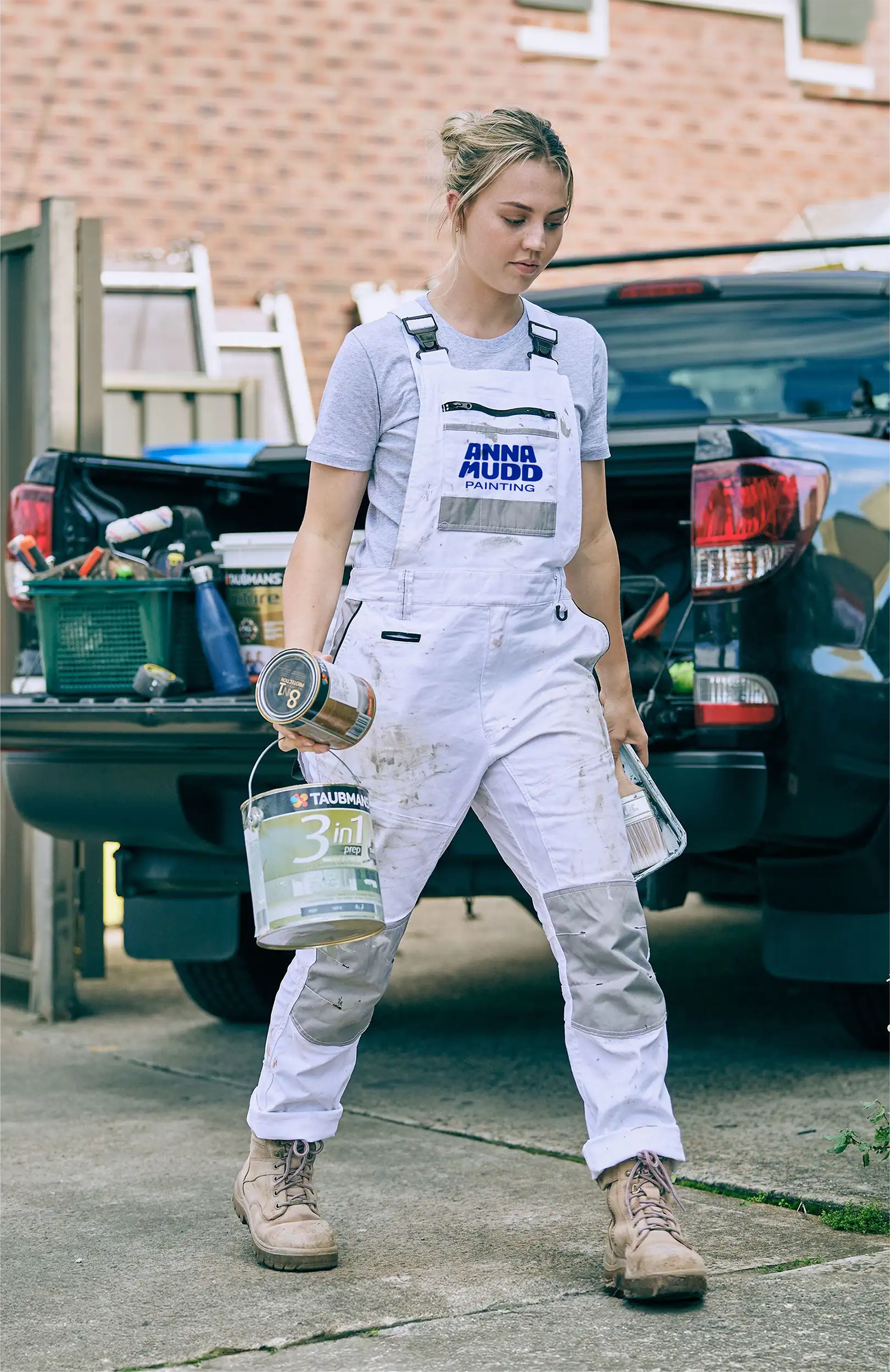 A painter wearing Anna Mudd Painting branded overalls