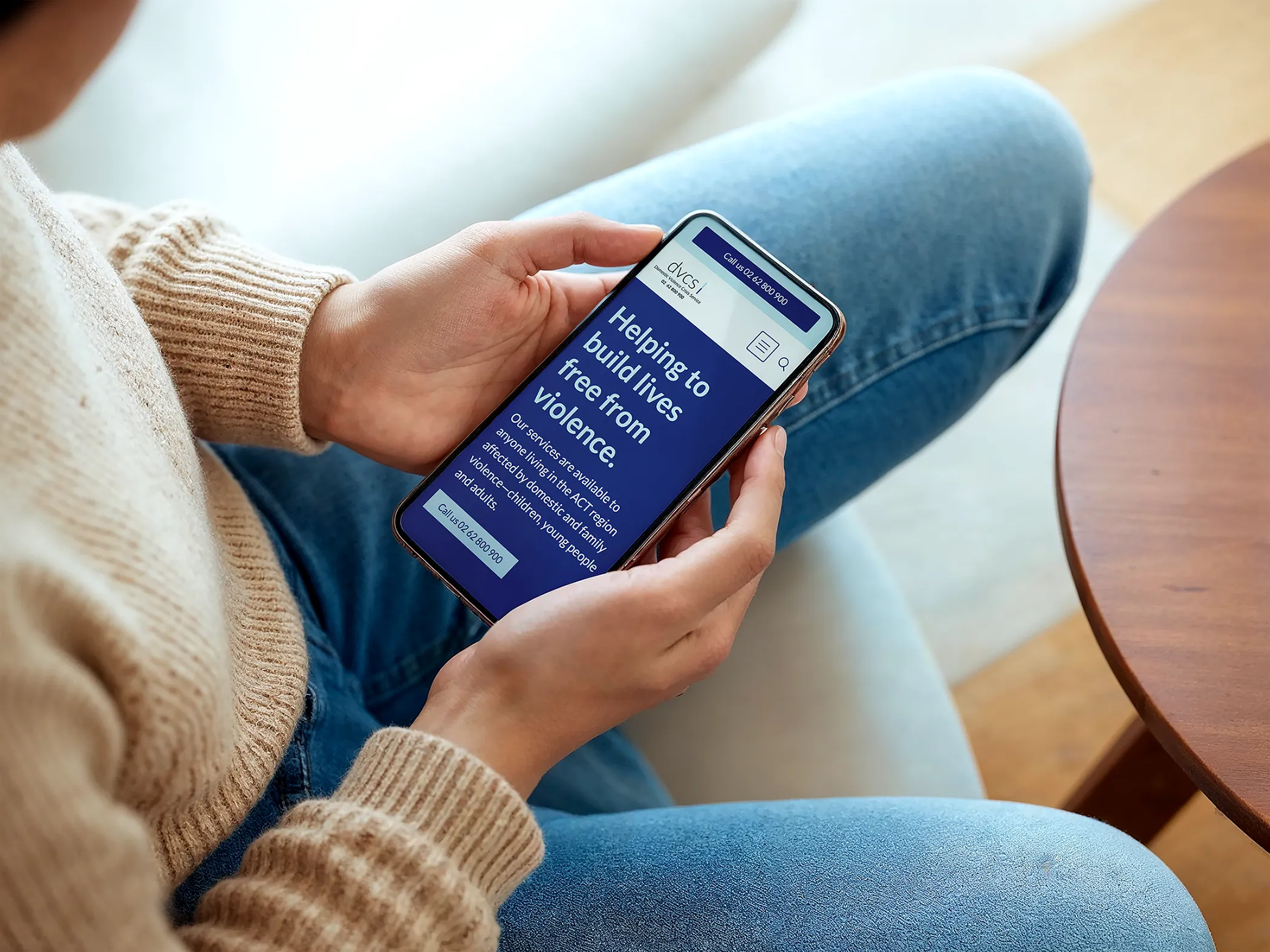 Woman sitting cross-legged, holding her phone which has the DVCS homepage open