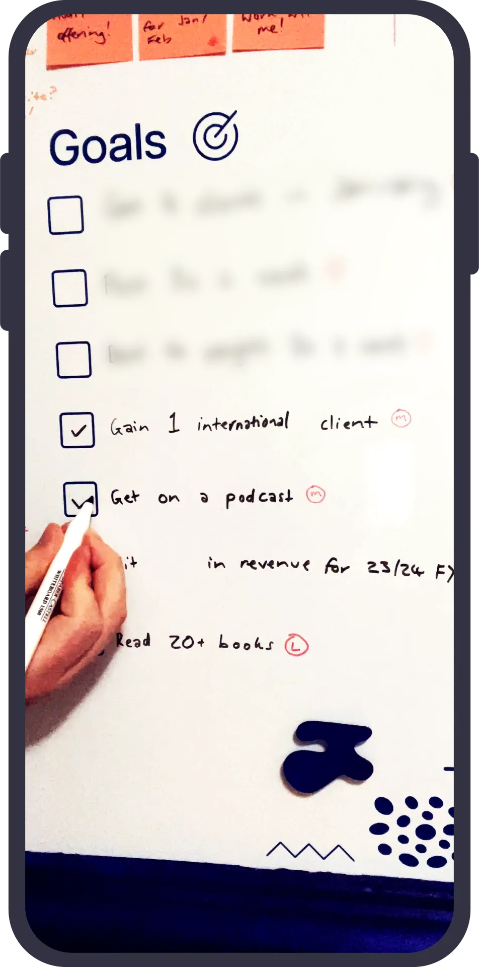 Whiteboard with goals. 'Gain 1 international client' and 'Get on a podcast' are checked.