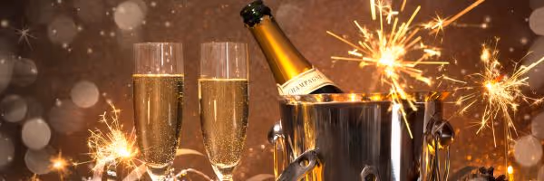 Two champagne flutes and a champagne bottle in an ice bucket surrounded by sparklers with bokeh light effects.