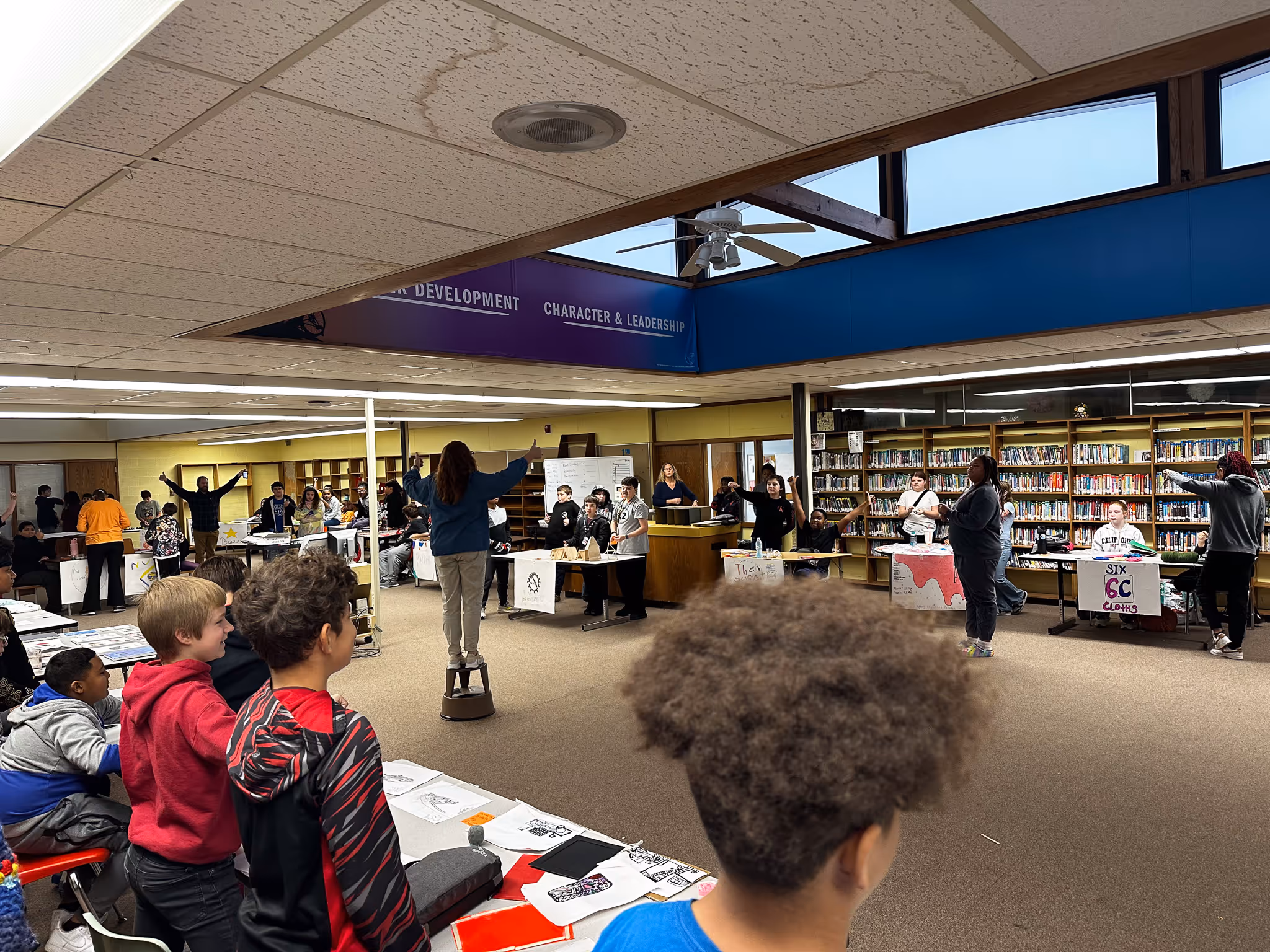A teacher addressing a large circle of students in the library.
