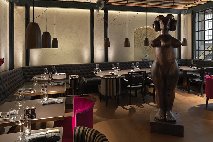 Hotel Widder in Zürich, das Restaurant mit dunklen Sitzbänen und kunstvoller großer Statue in der Mitte des Raums