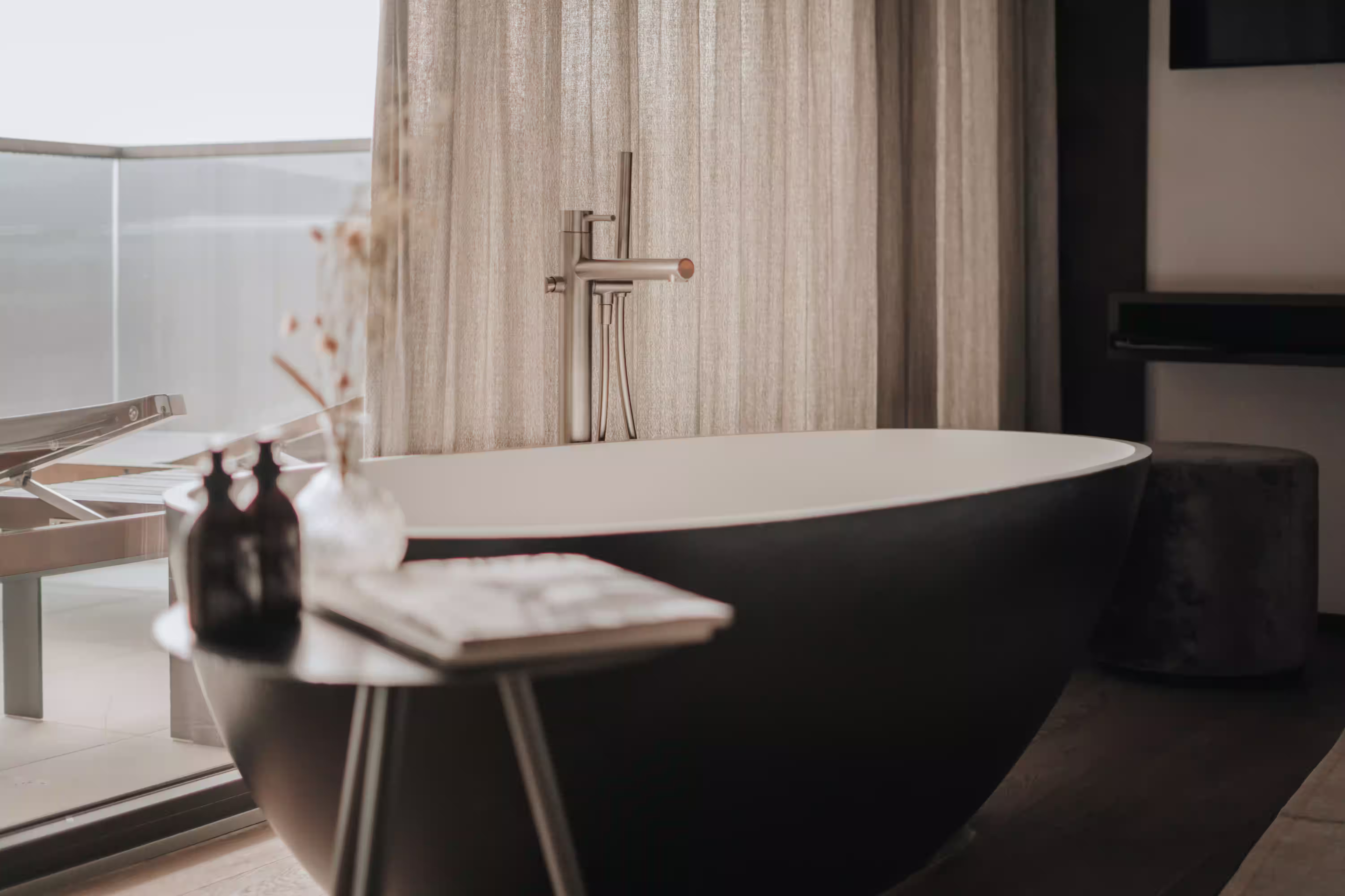 DAS PARADIES – Freistehende schwarze Badewanne mit Edelstahlarmatur vor bodenlangem Vorhang