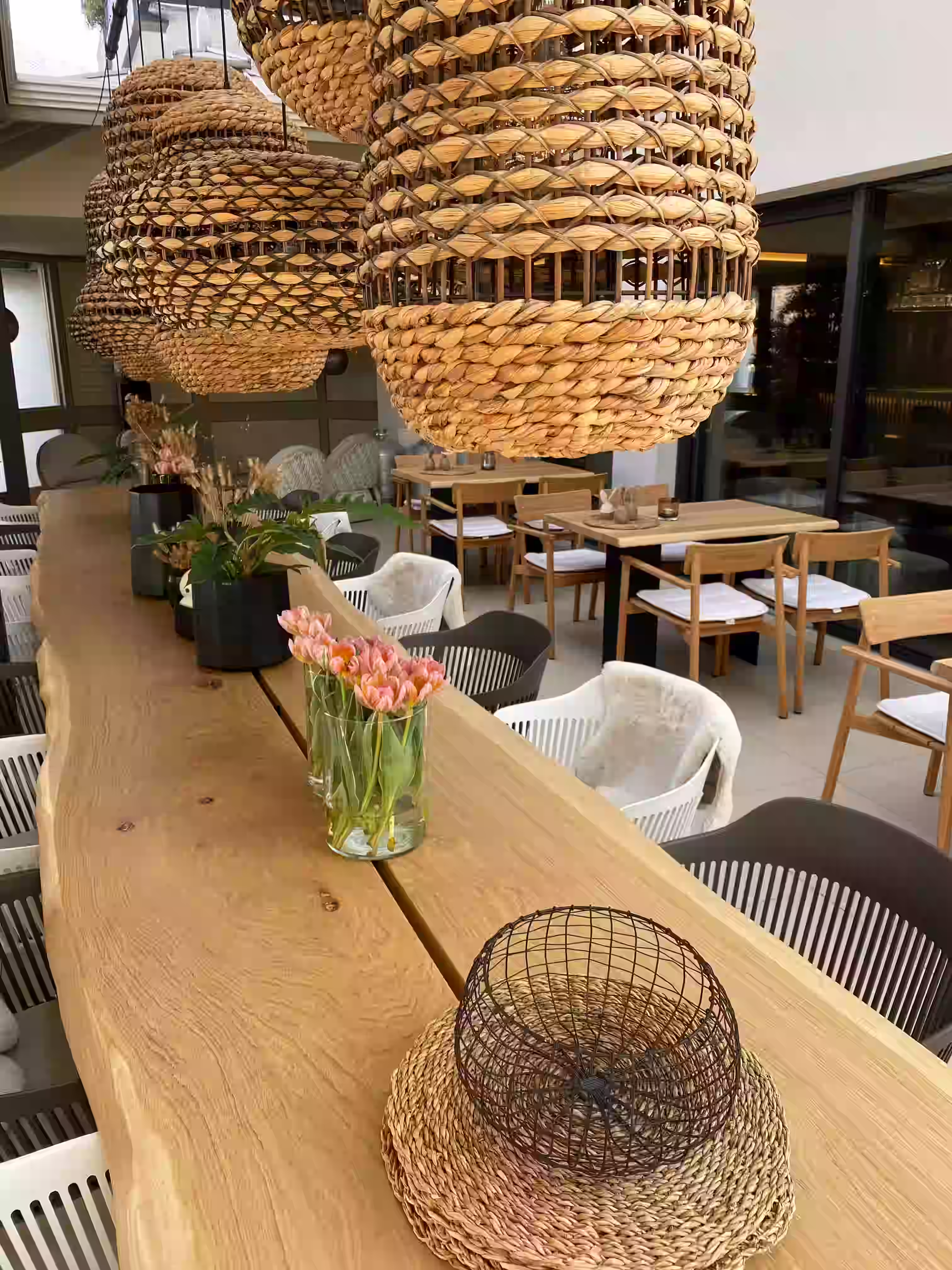 DAS PARADIES – Essbereich mit Baumkantentisch, Tulpenstrauß und geflochtenen Hängeleuchten; helle Holzstühle und Terrassenbereich im Hintergrund
