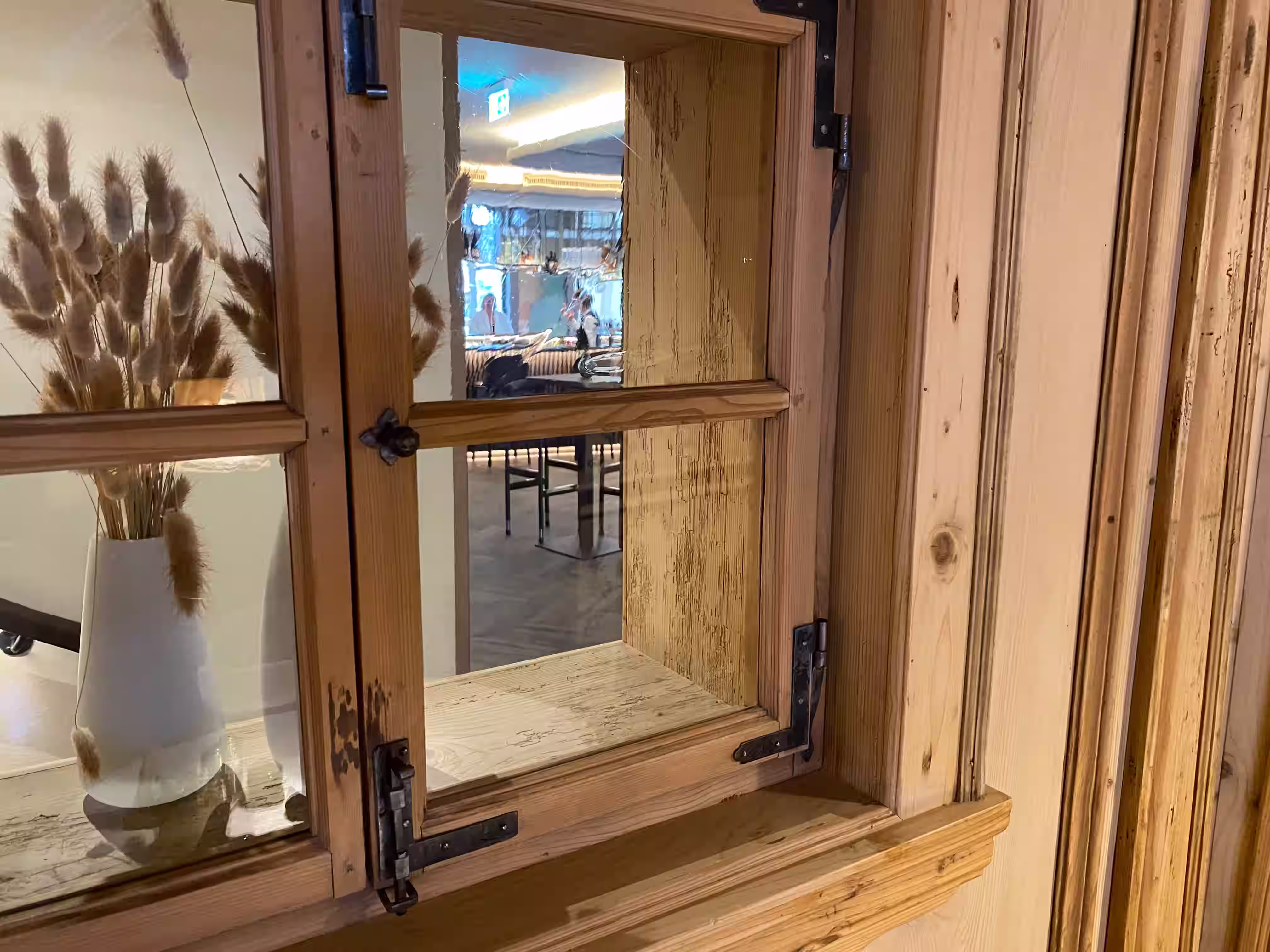 DAS PARADIES – Rustikales Holzfenster mit Eisenbeschlägen und Trockenblumen; Durchblick auf den Barbereich