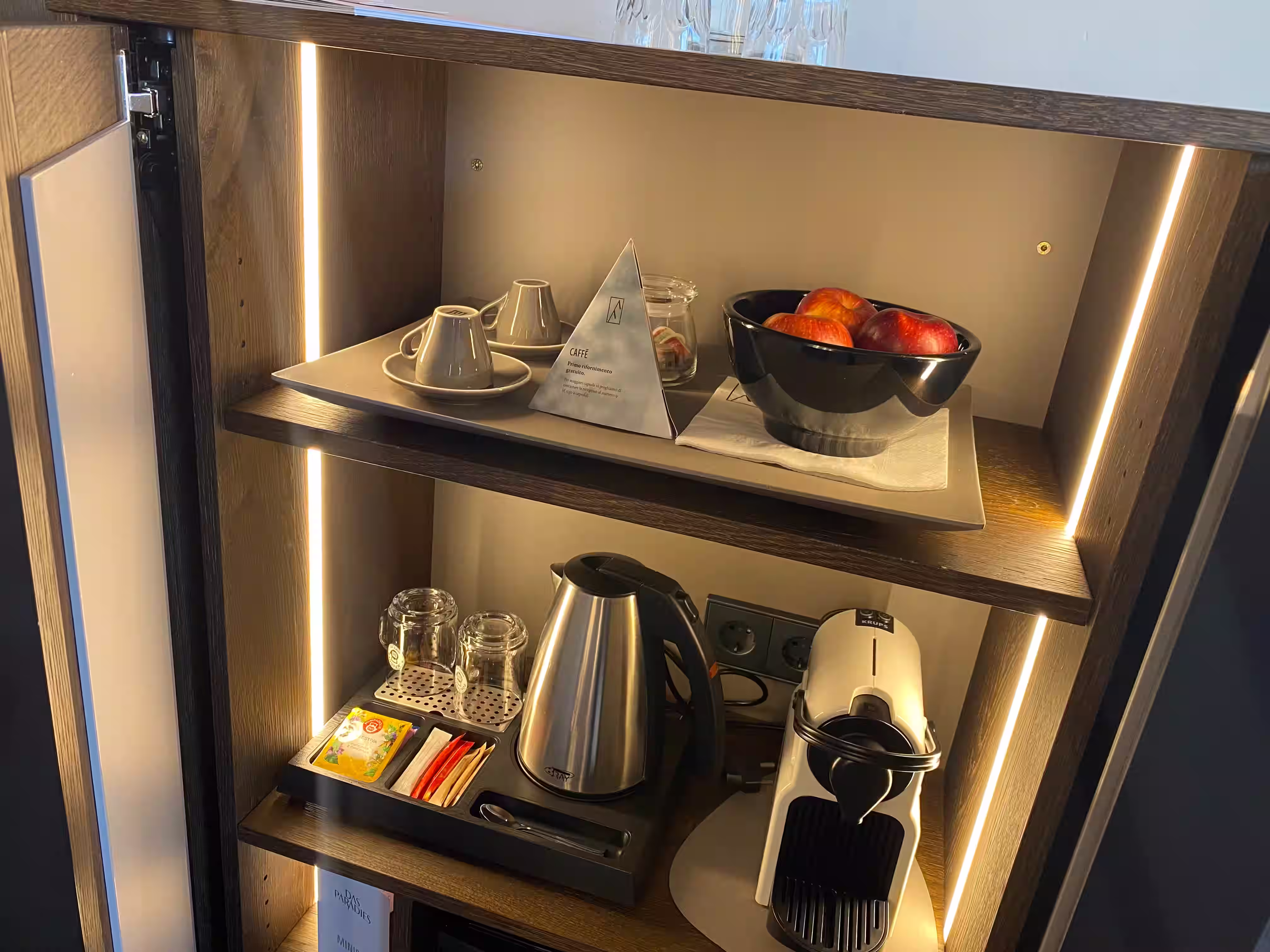 DAS PARADIES – Beleuchtetes Minibar-Element mit Nespresso-Maschine, Wasserkocher, Teetablett und Obstschale mit roten Äpfeln